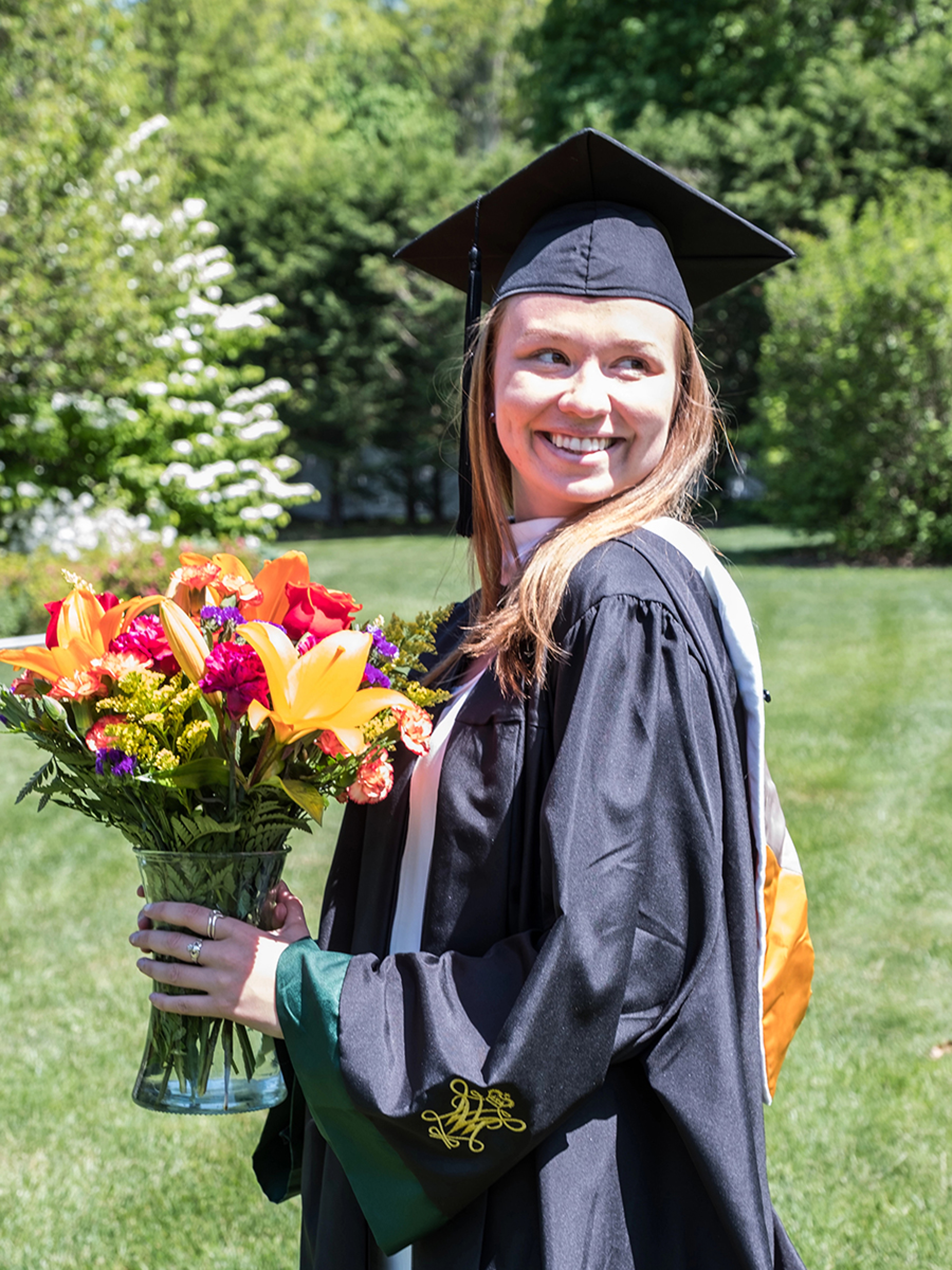 Woman wearing graduation cap and gown holding a bouquet of flowers.