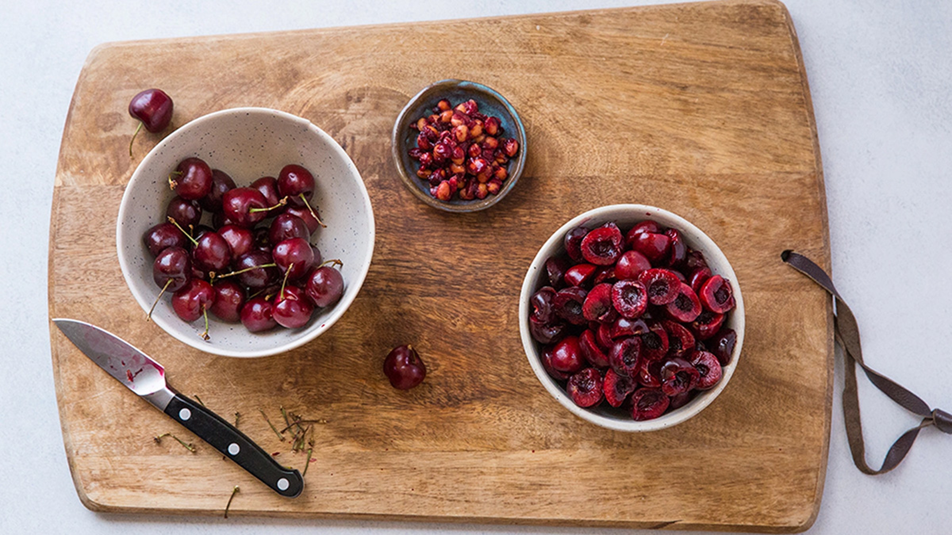 Process of making cherry compote with sliced and pitted cherries in bowls.