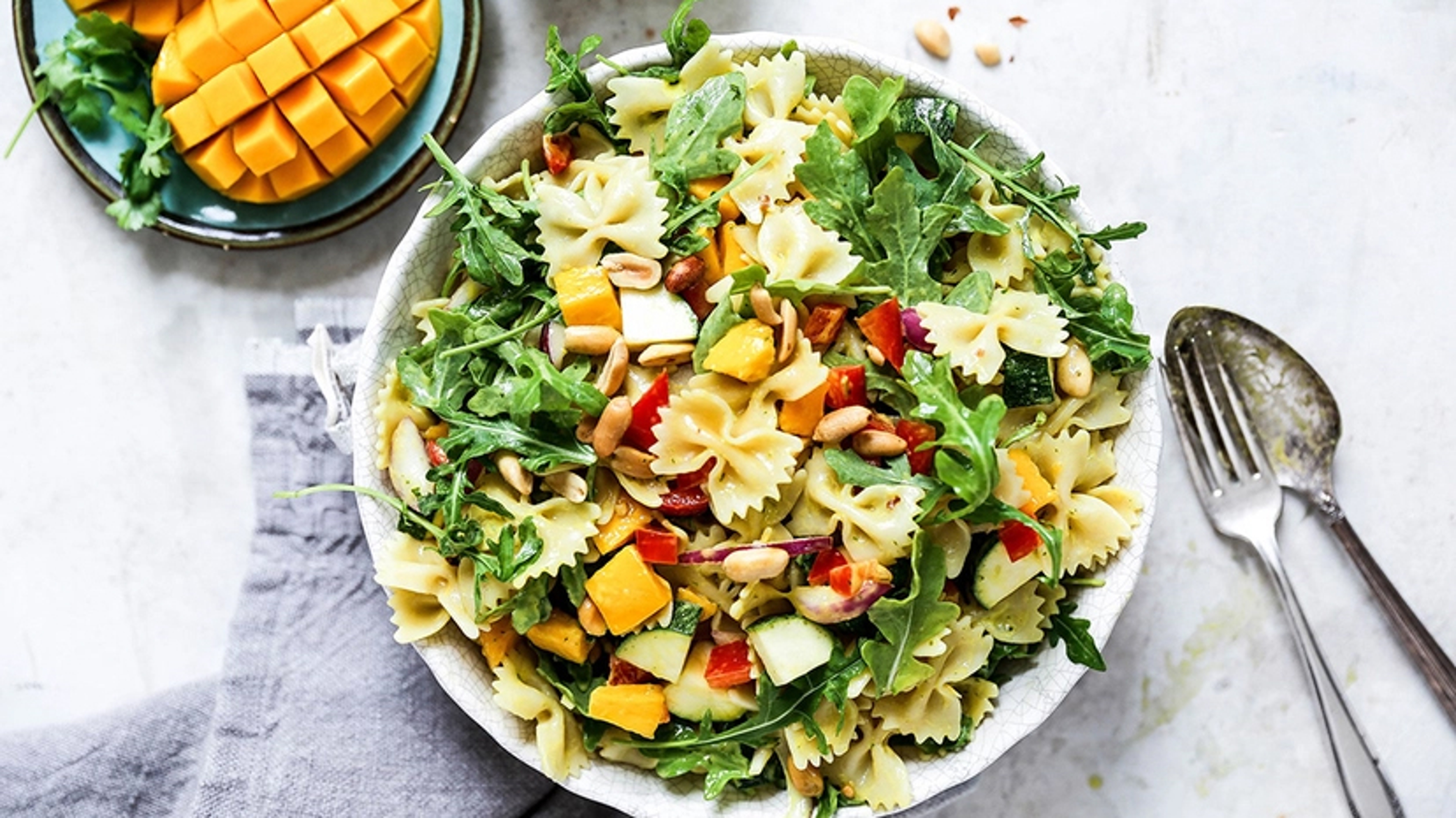 Bowl of pasta salad with mango and greens.