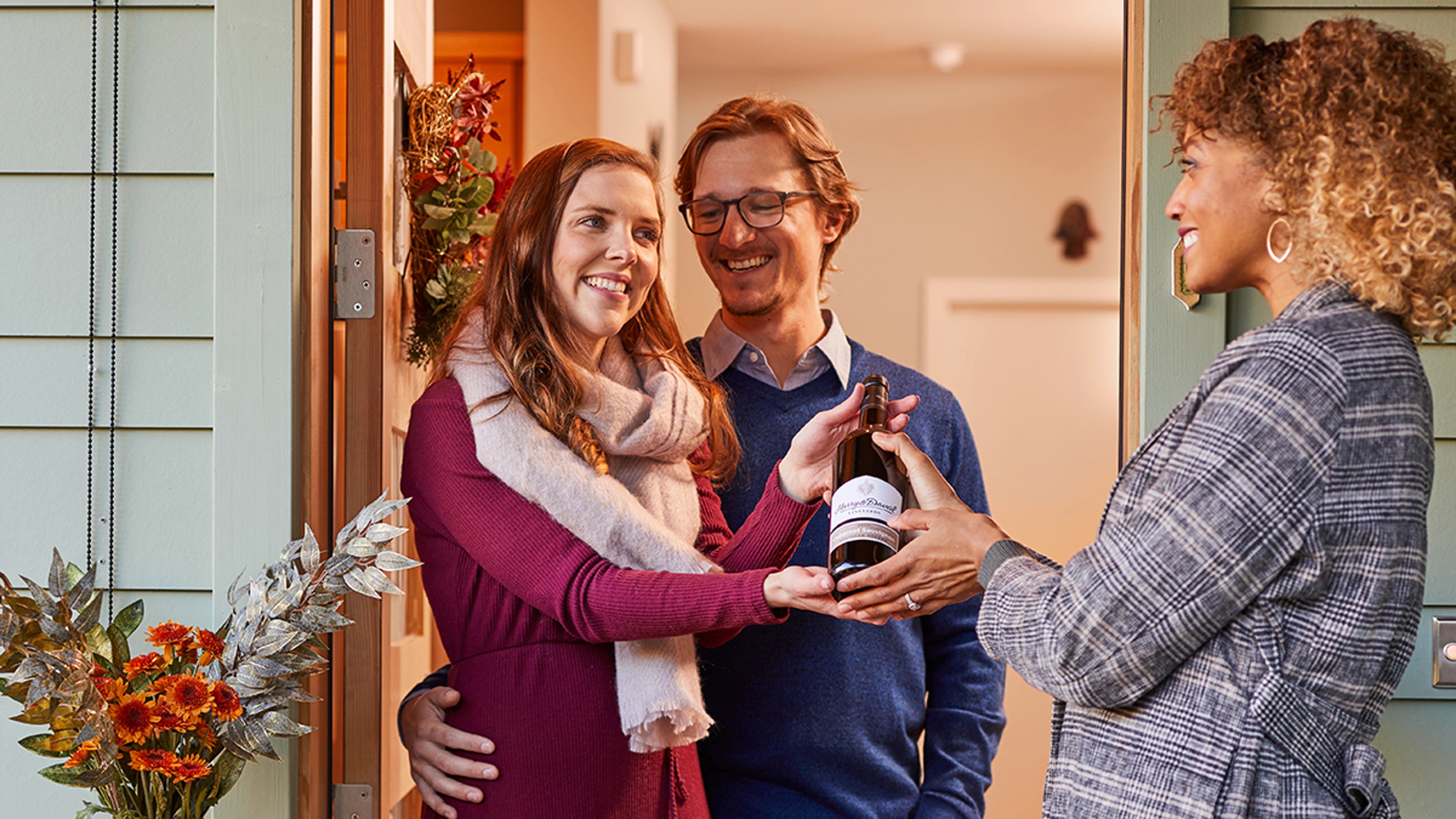 Dinner guest etiquette with a woman handing a couple a bottle of wine.