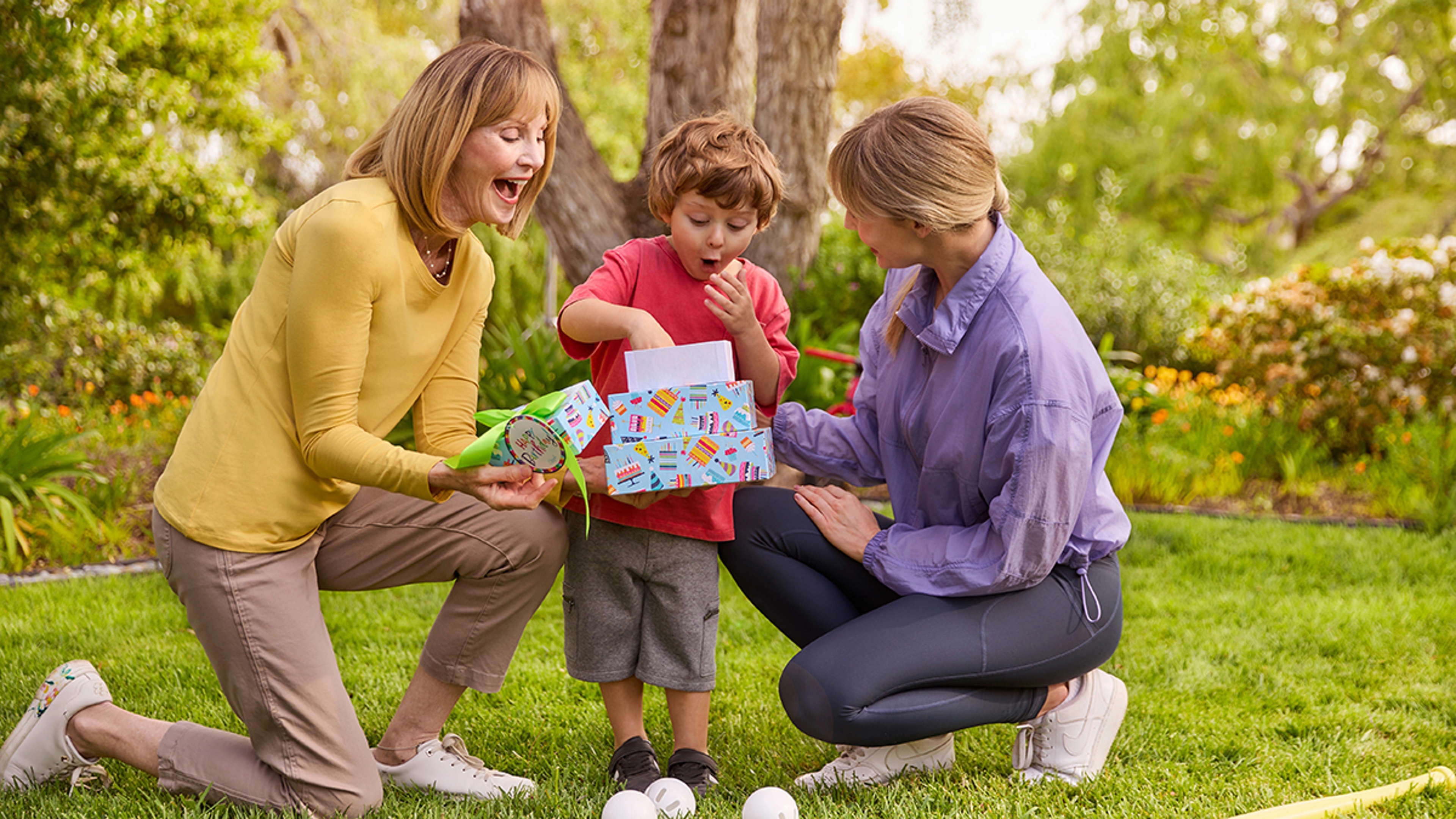 Young boy celebrating an August birthday and opening a gift outside.