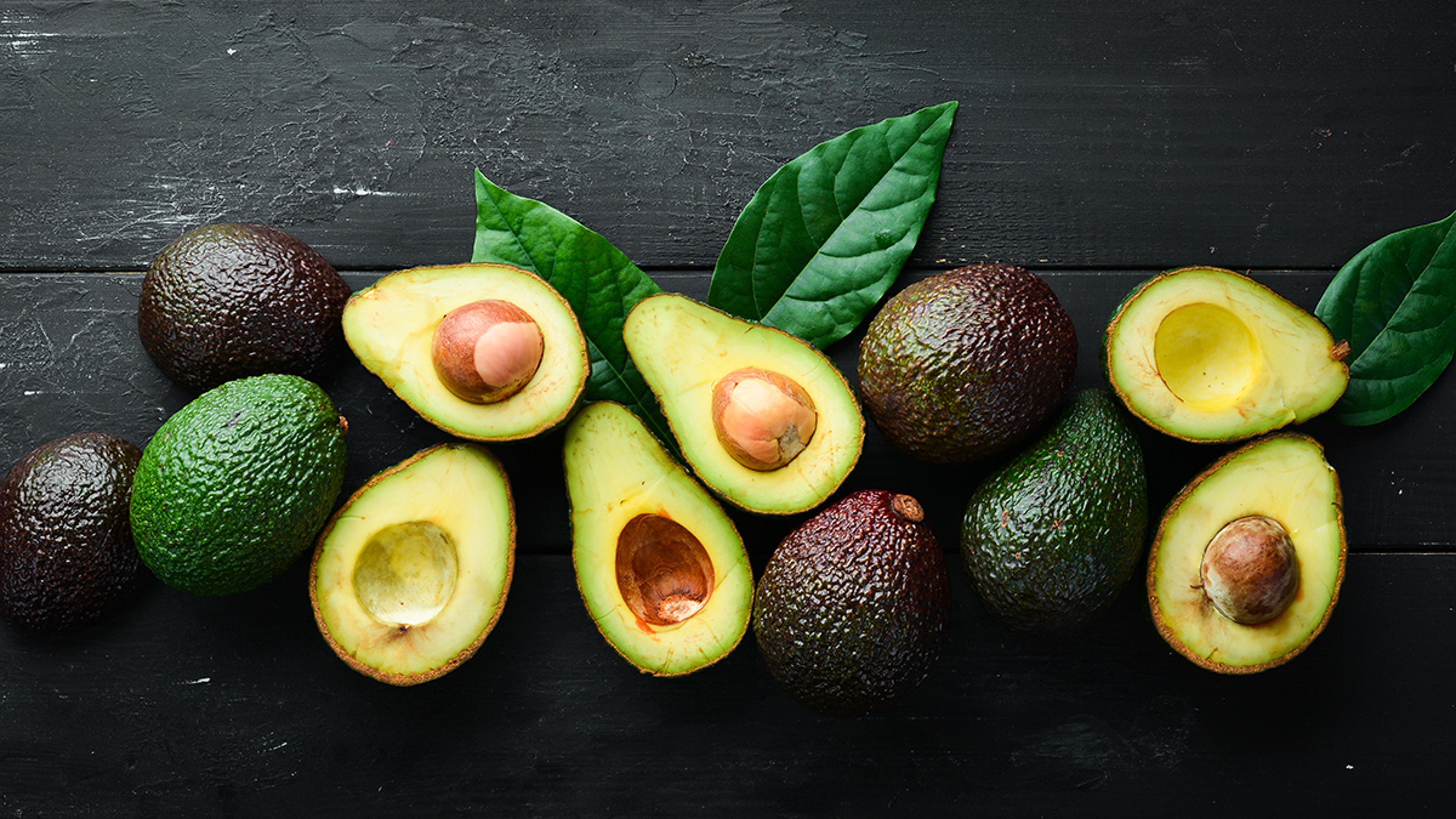 Fresh avocado with leaves on a black background. Top view. Free space for your text.