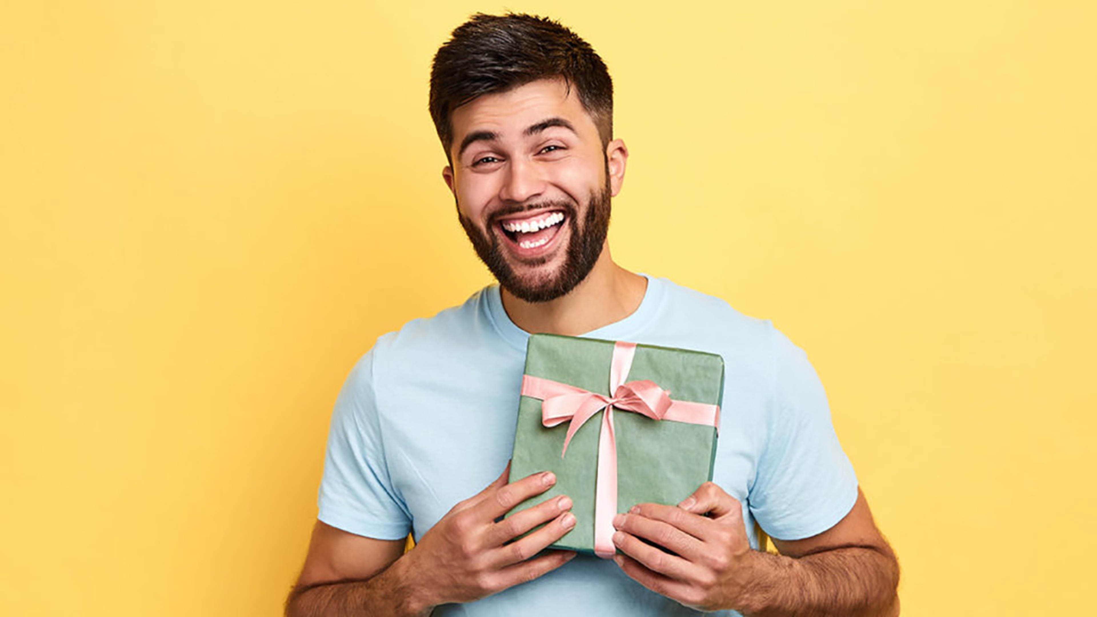 handsome bearded overjoyed man wearing casual clothes holding present box standing isolated over yellow background,Birthday party. celebration, happiness, best present from girlfriend