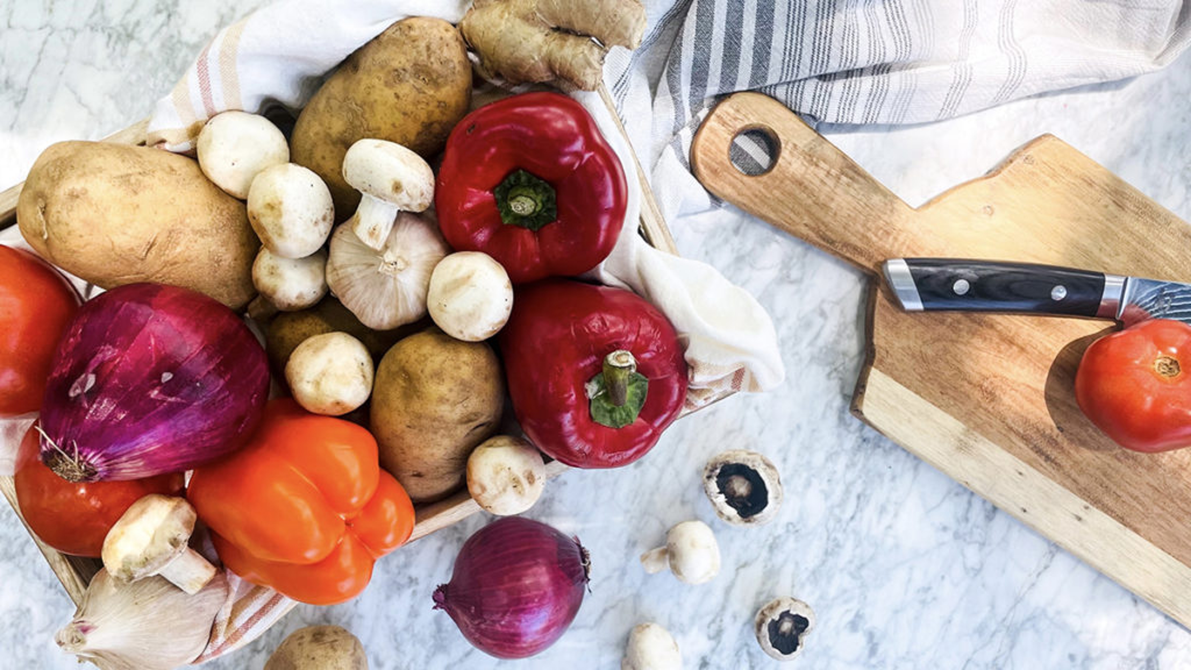 Crate of vegetables for steak kebabs next to a cutting board.