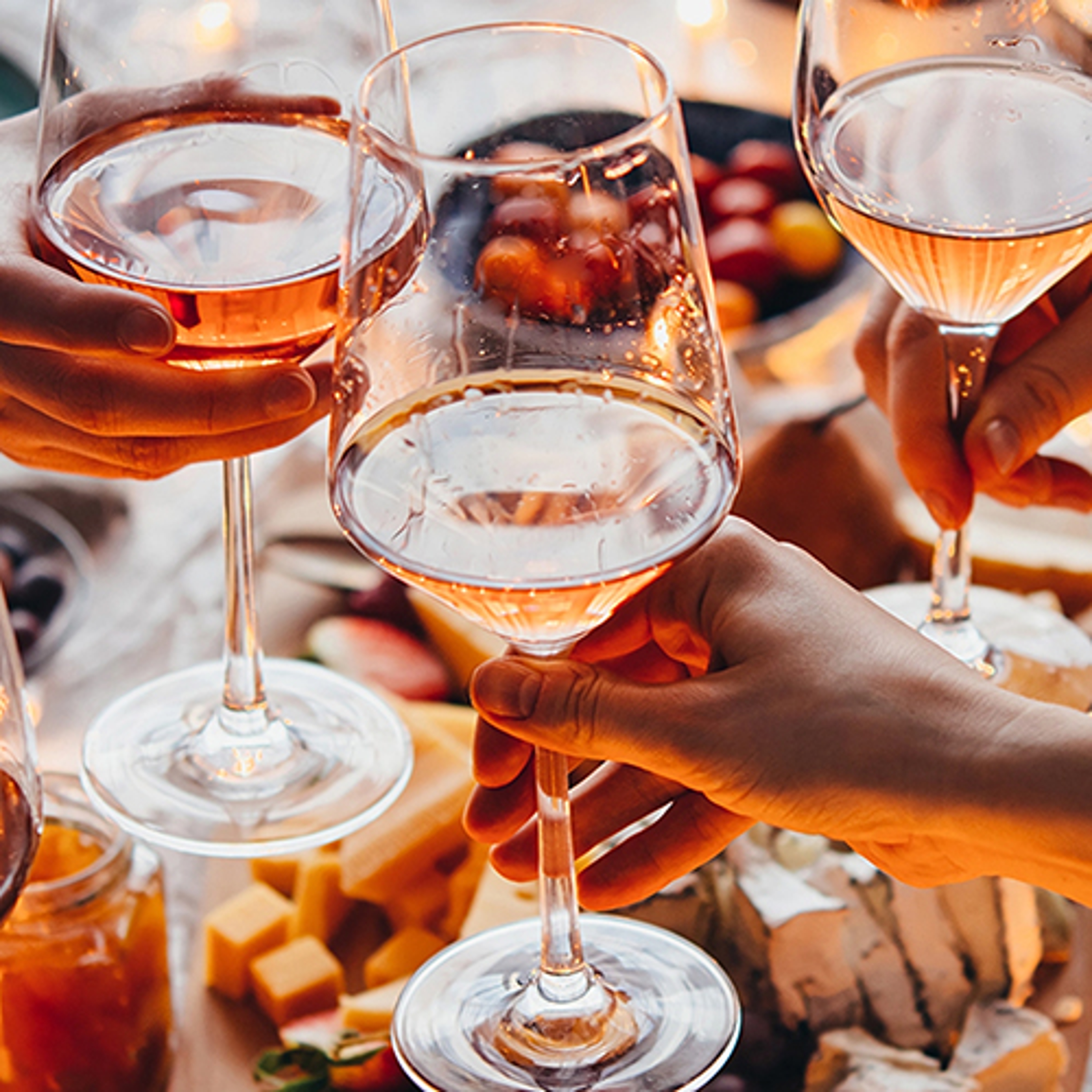 Glasses of rosé wine getting clinked together over a table of food.