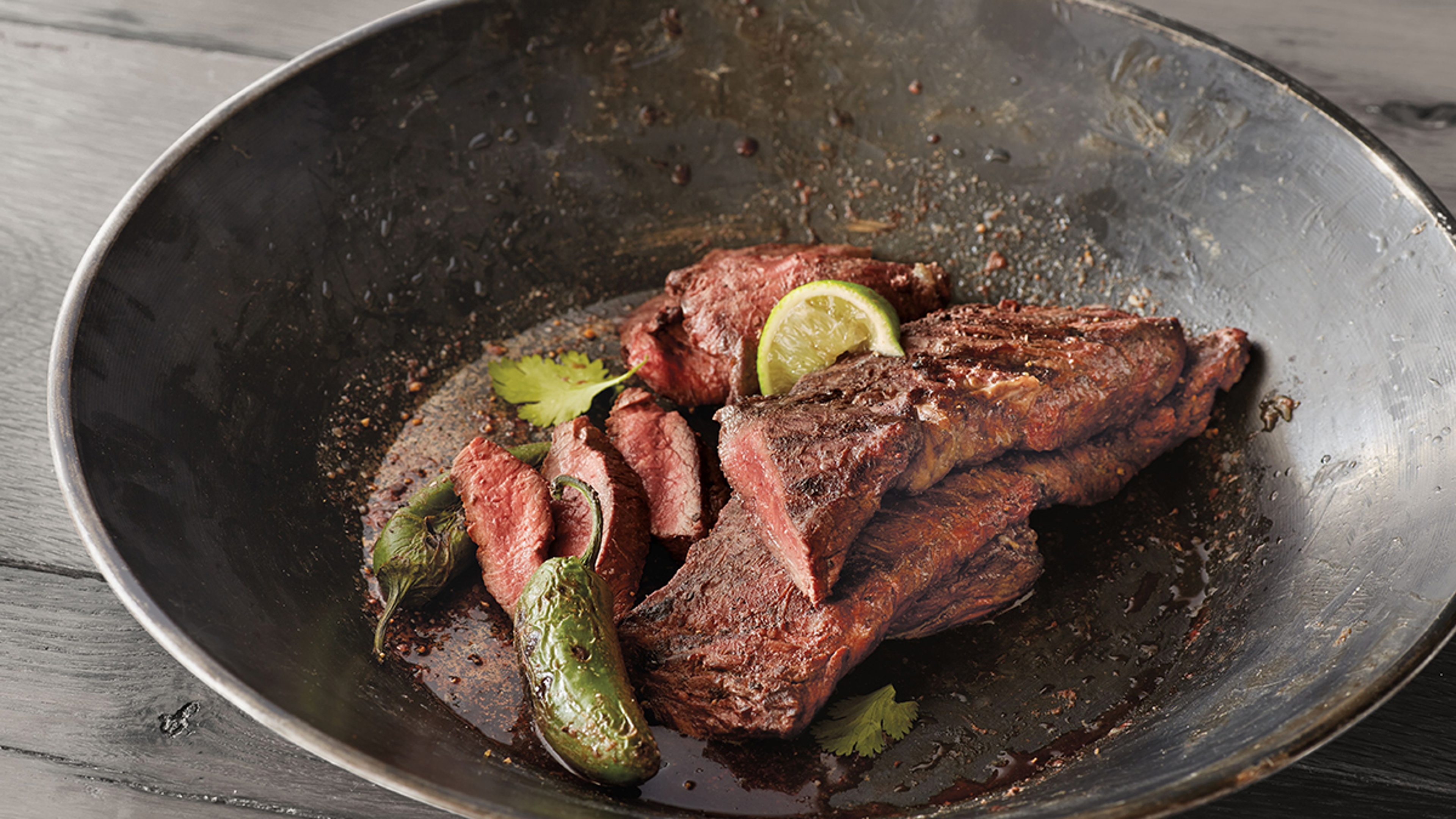 Bowl of skirt steak with limes and jalapenos.