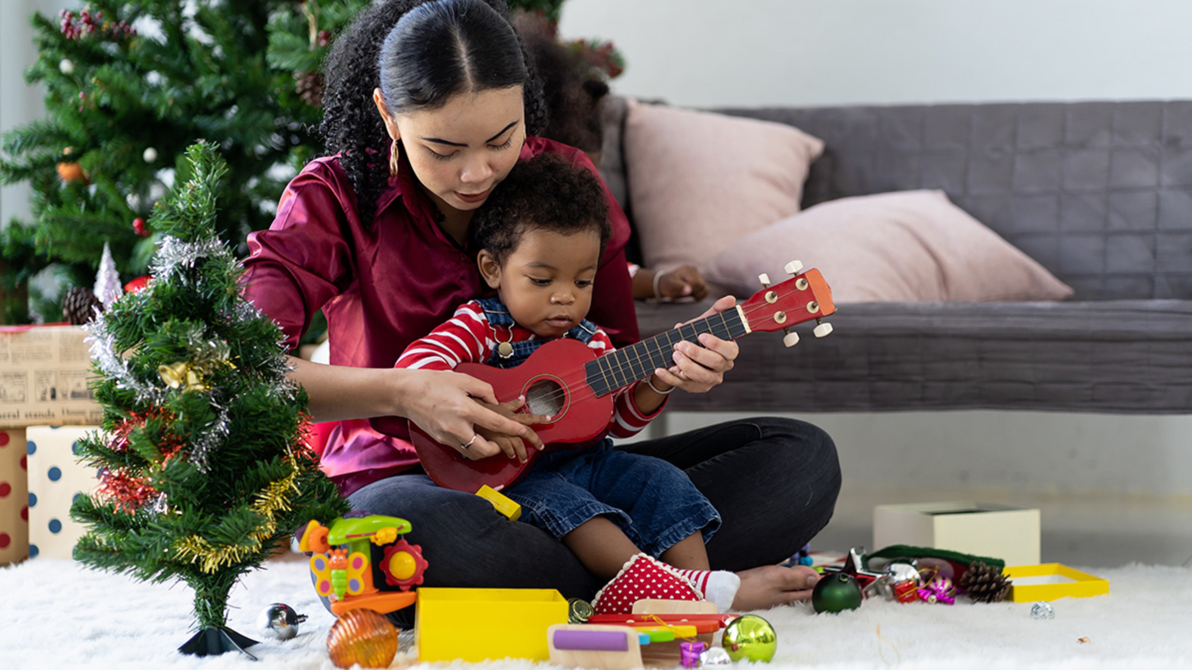 Ways to say merry Christmas mother with son in her lap playing ukulele with christmas decorations in the background.