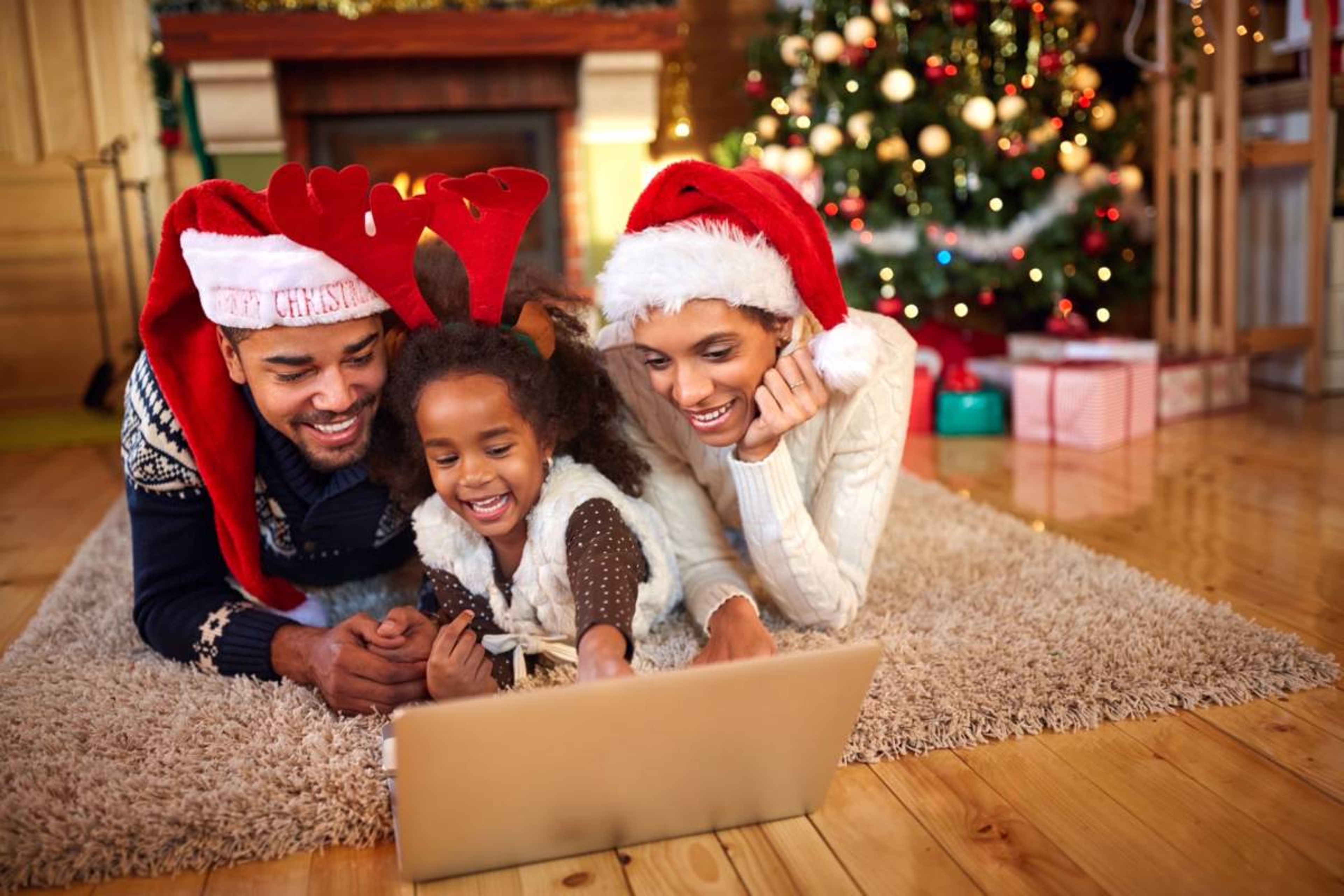 Family celebrating christmas wearing matching hats while laying on the floor in front of a laptop