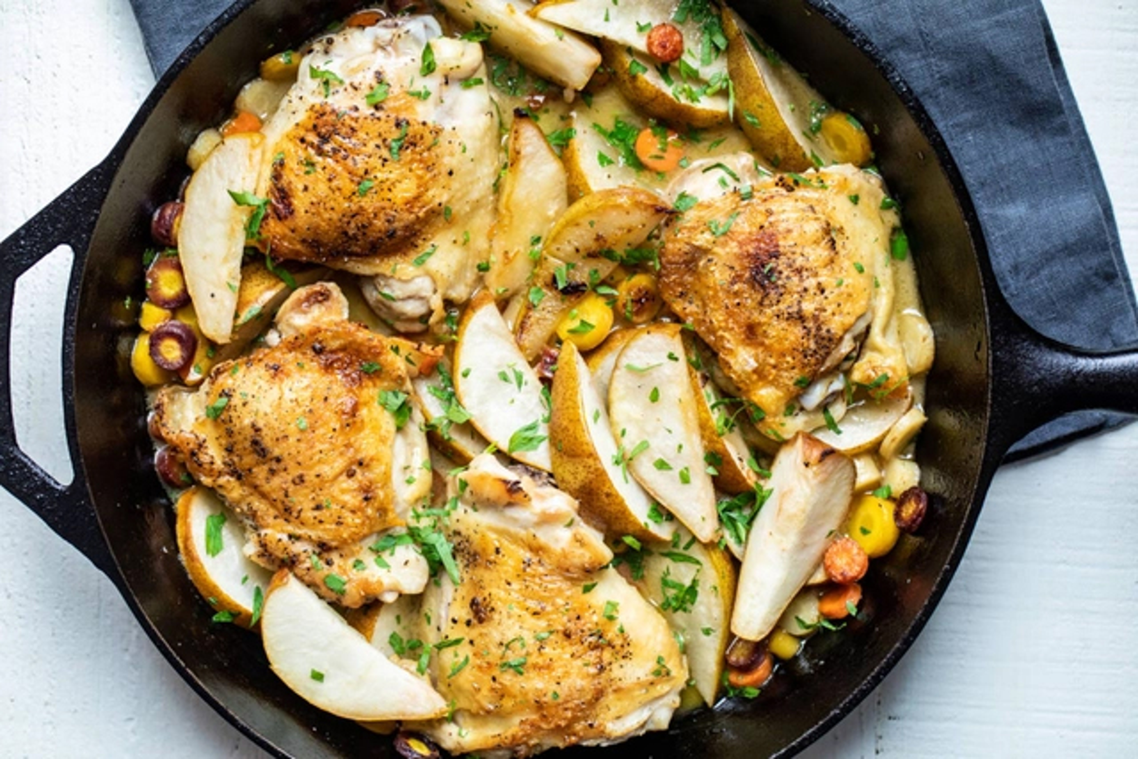 Cast iron skillet with chicken, pears, and vegetables.