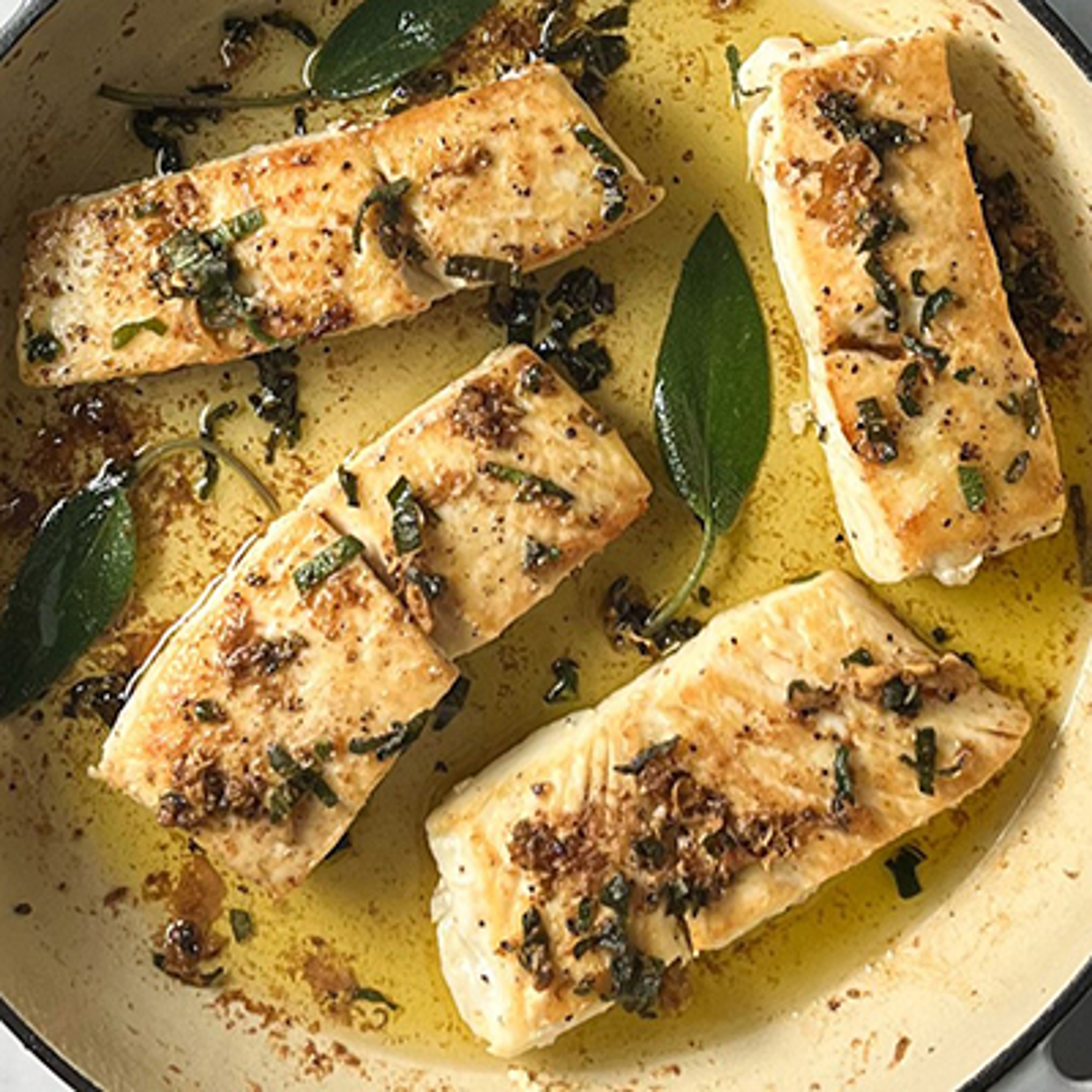 Summer fish recipes with a closeup of several pieces of cooked halibut in a pan with butter and sage.