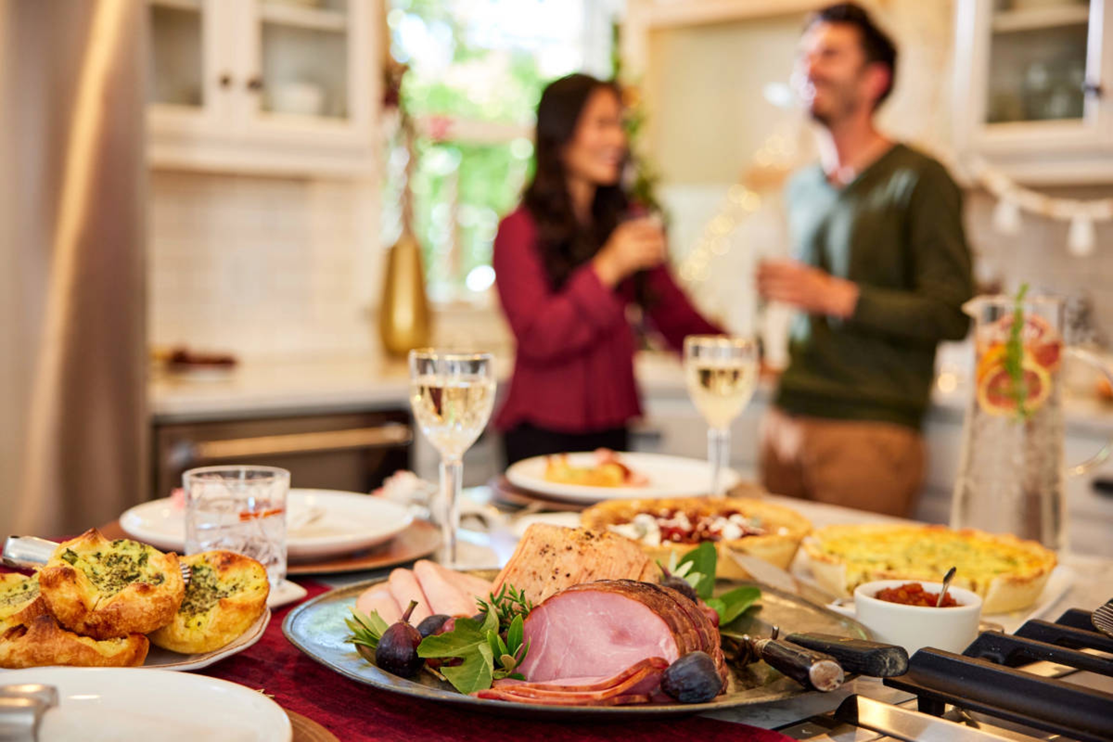 Thanksgiving host tips with a display of food and drinks on a counter with two people talking in the background.