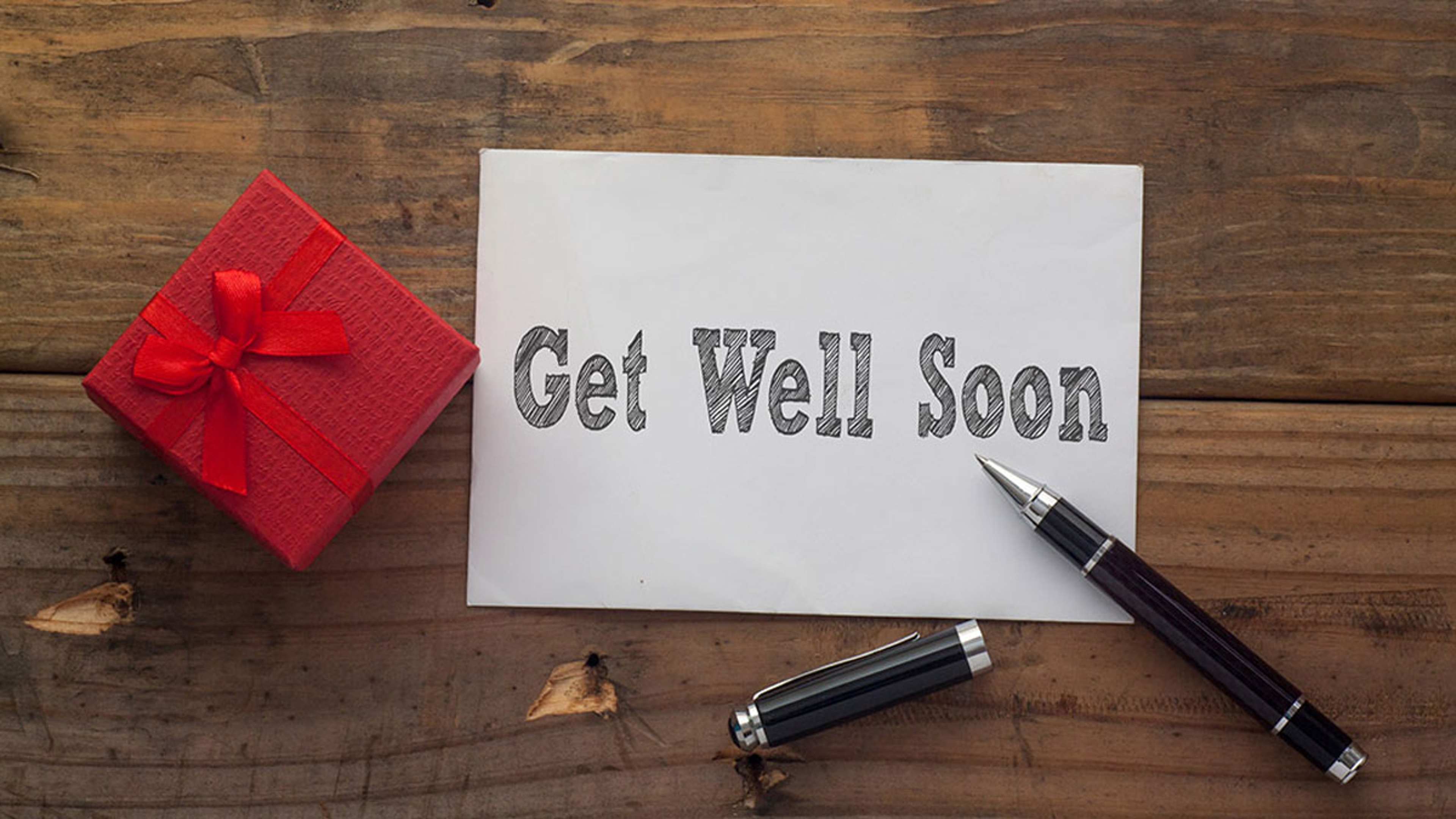 Article Cards Featured Image Get Well Soon written on paper with pen,red gift box and wooden background desk.