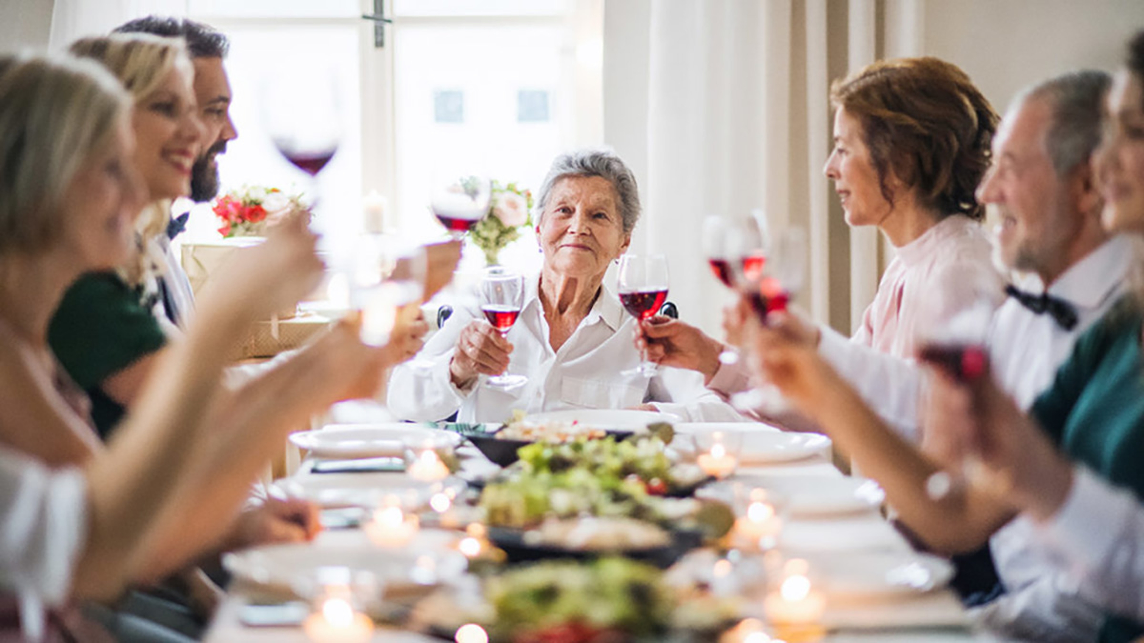 Birthday party idea for seniors with an older woman raising a glass of wine at a full dinner table.