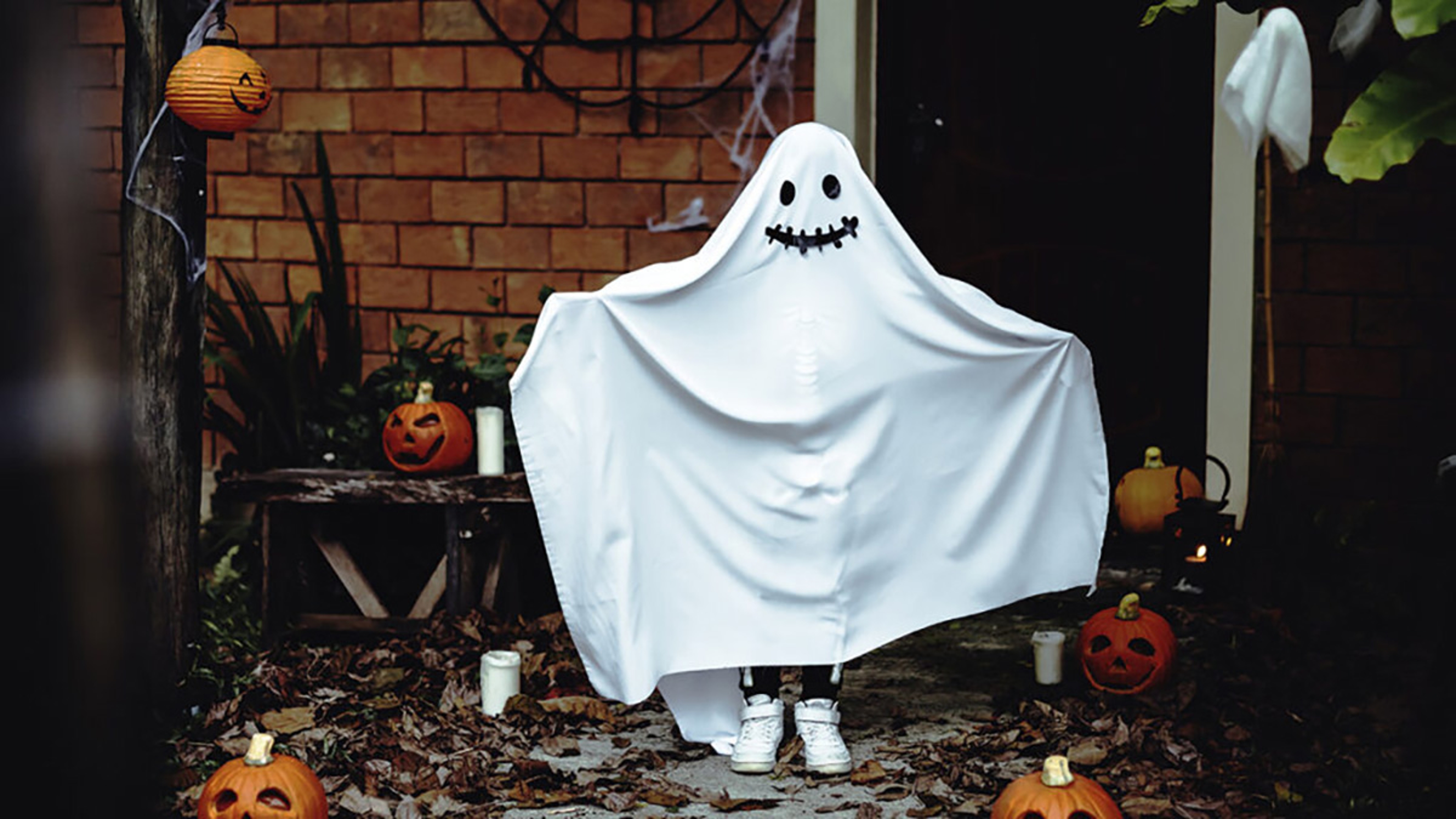 Child in a ghost costume on a front porch.