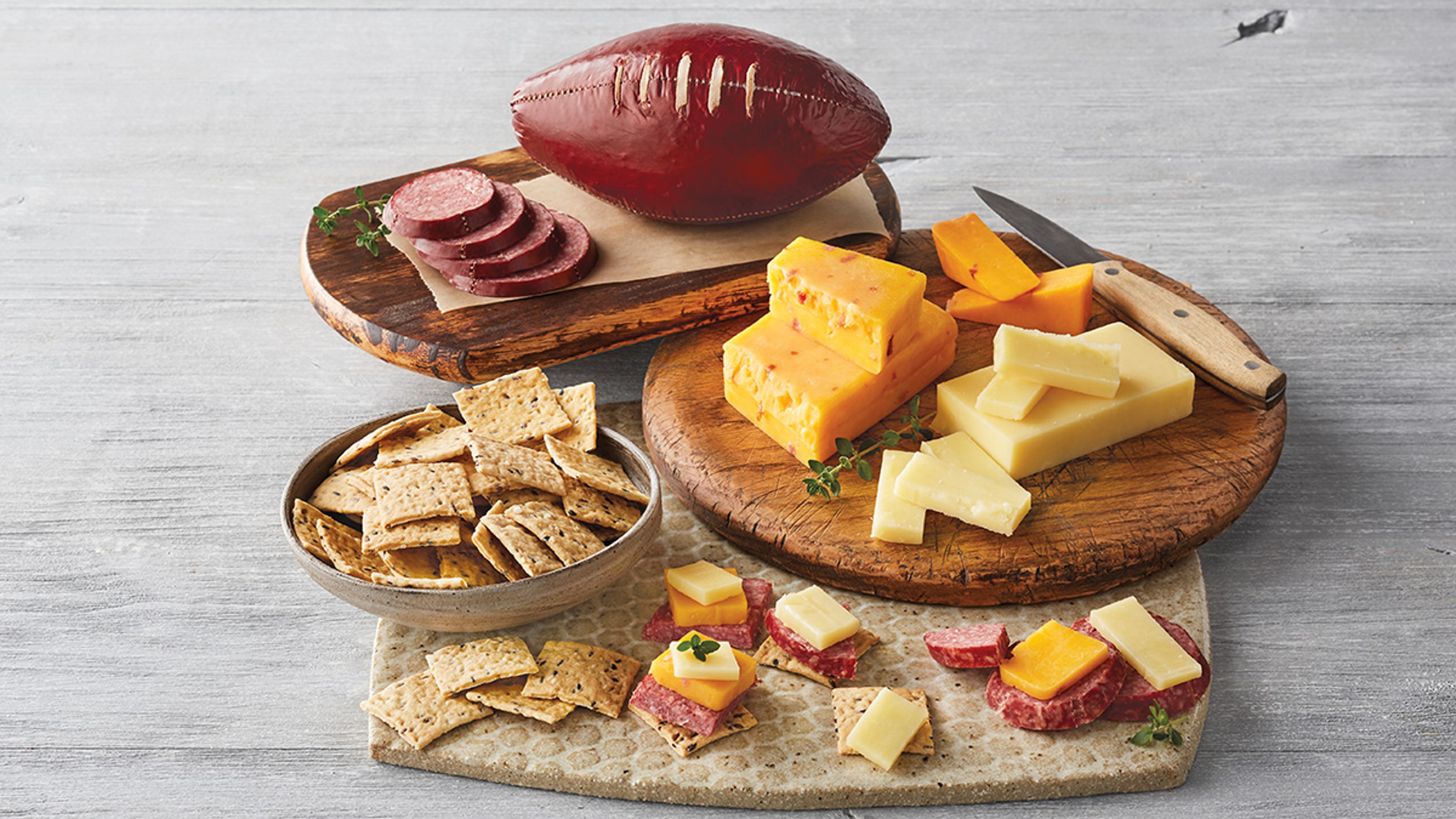 Football sausage on a cutting board with several different types of cheese and crackers.