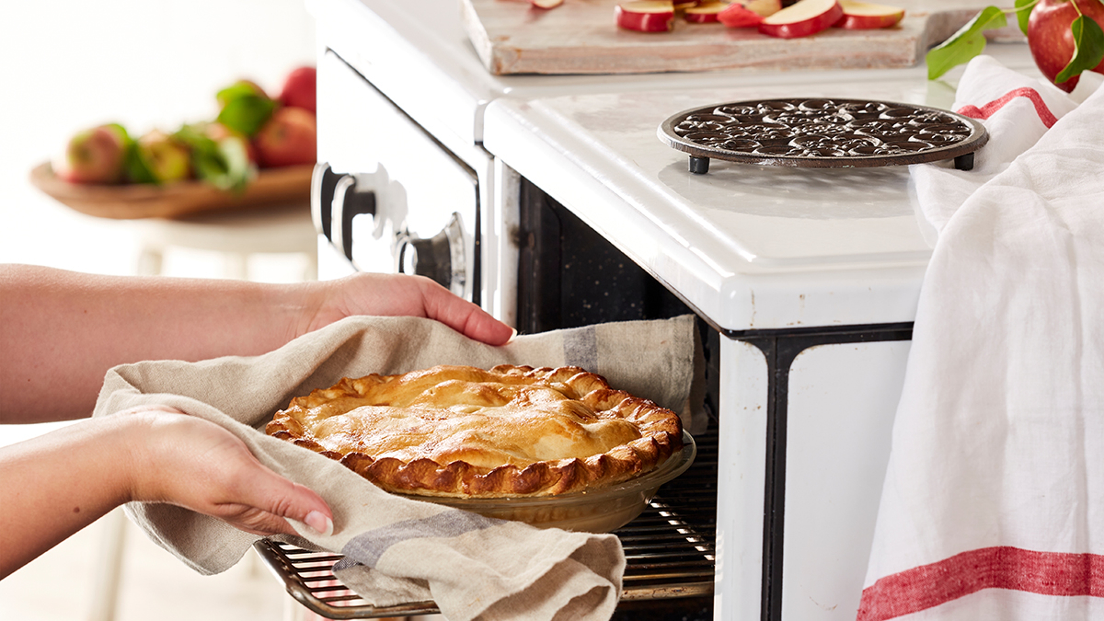 Hands pulling apple pie out of an oven.