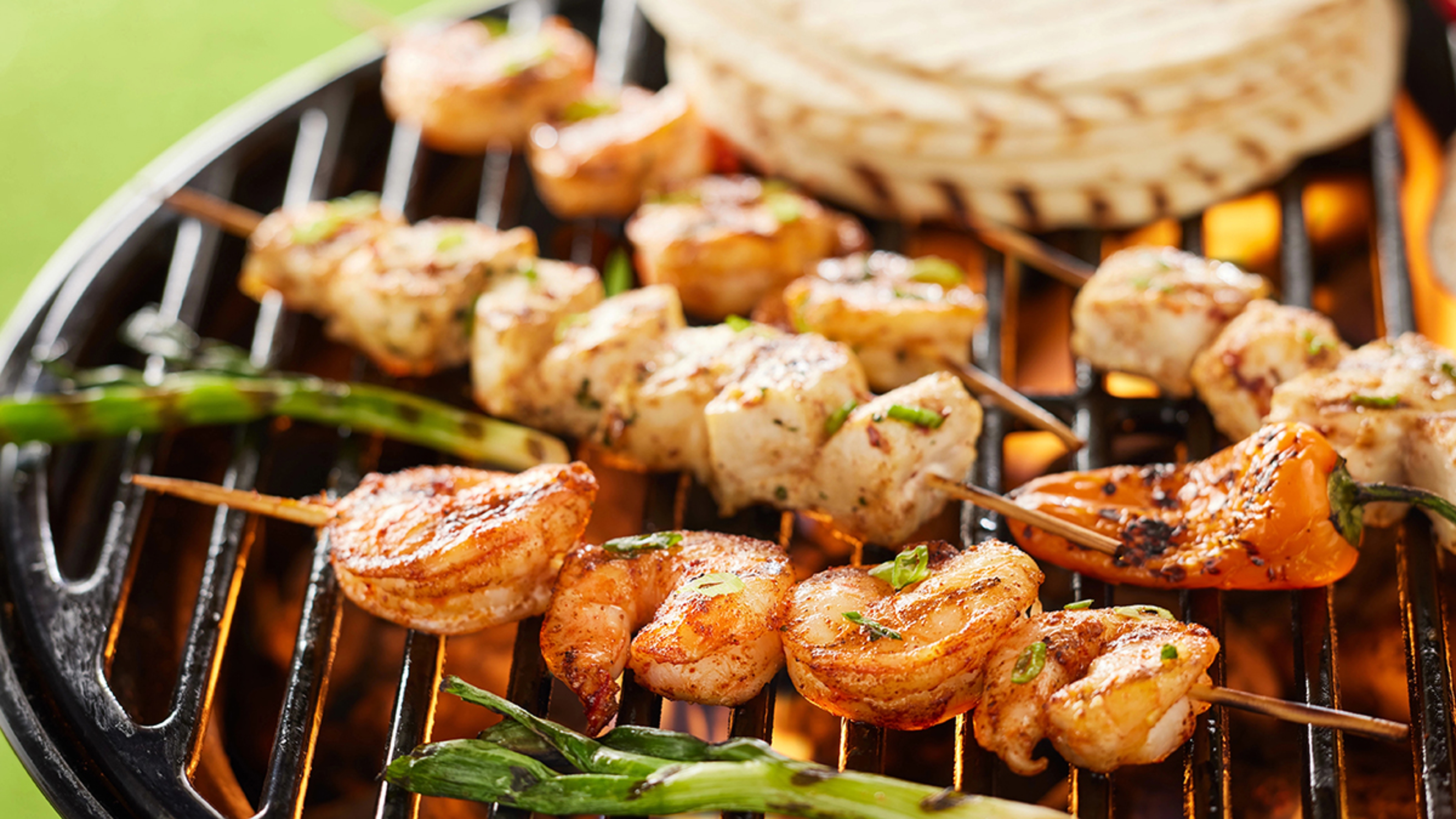 Close up of shrimp and fish skewers grilling.