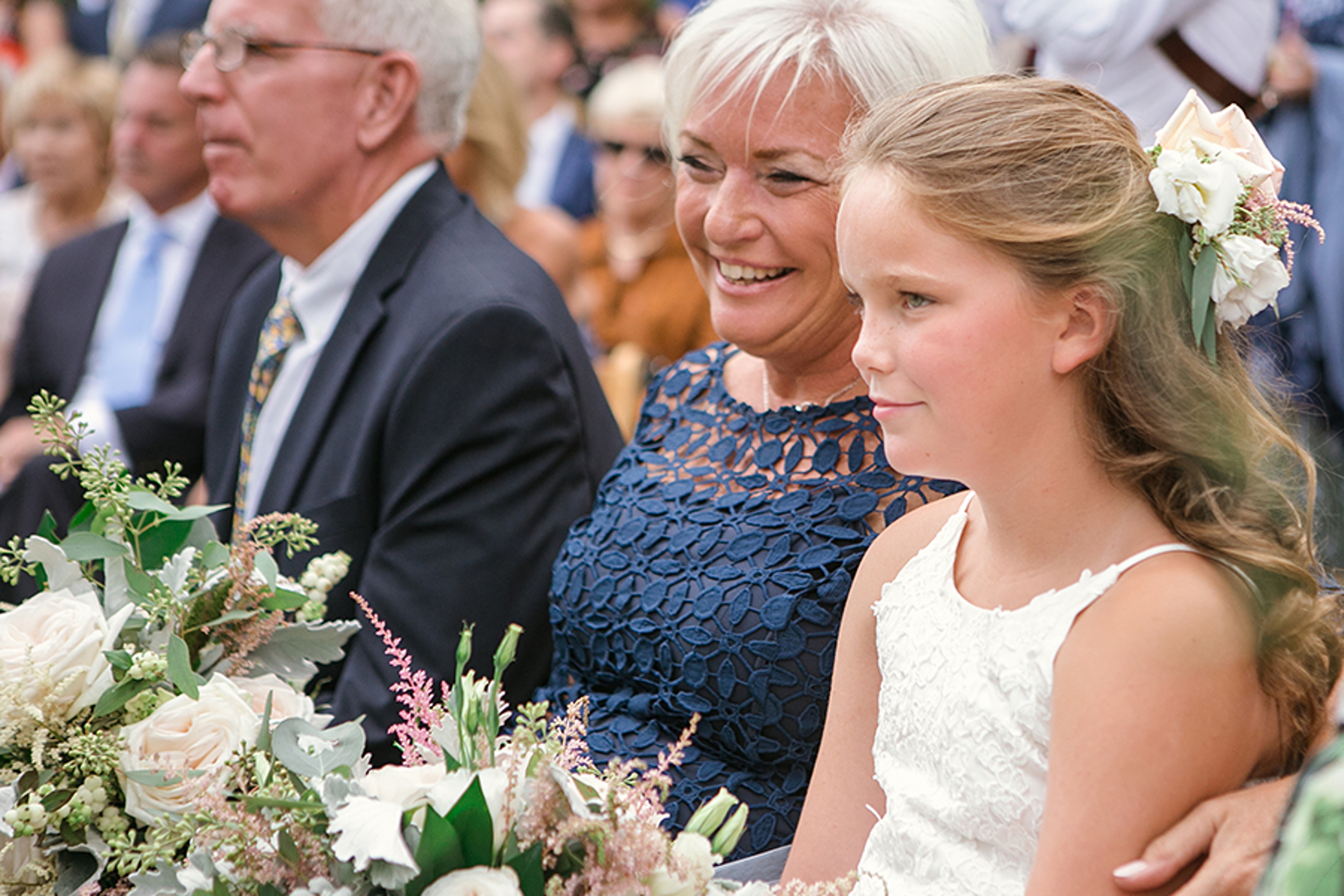 Mother sitting with flower girl at a wedding as she holds a bouquet of flowers