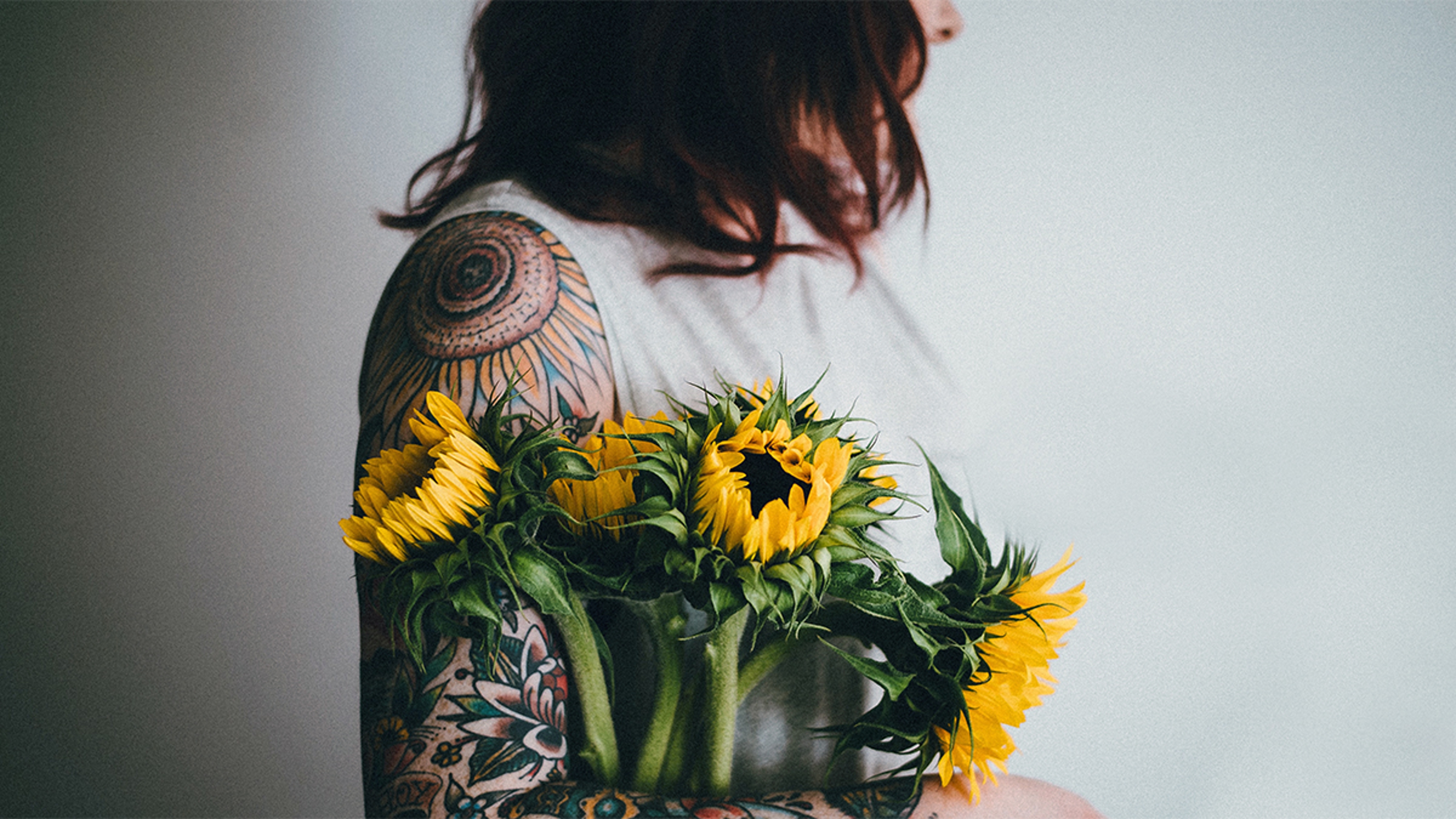 Article Cards Featured Image A woman holding sunflowers next to her flower tattoo