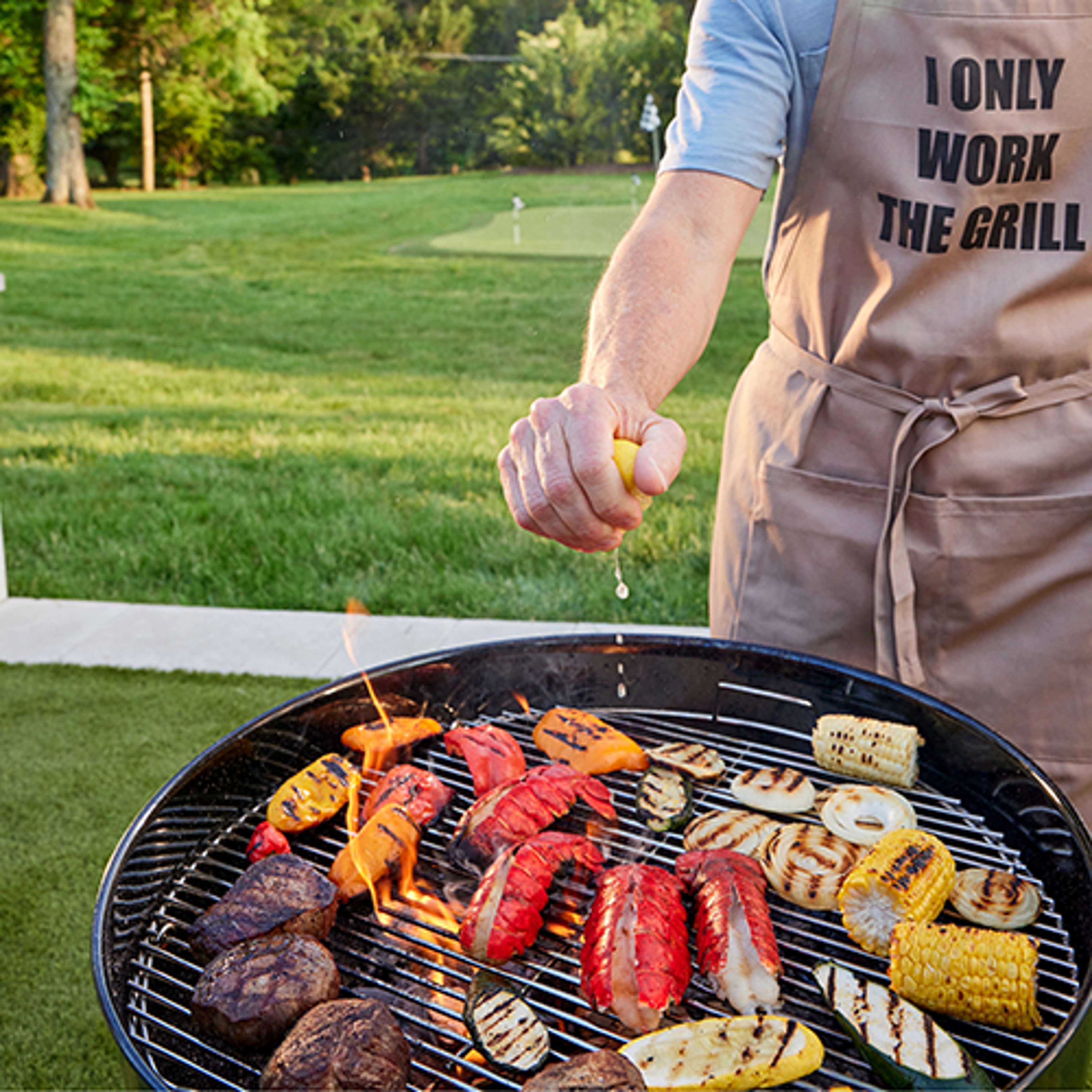 Ode to the lobster with a hand squeezing lemon over a grill with lobster, vegetables, and meat.