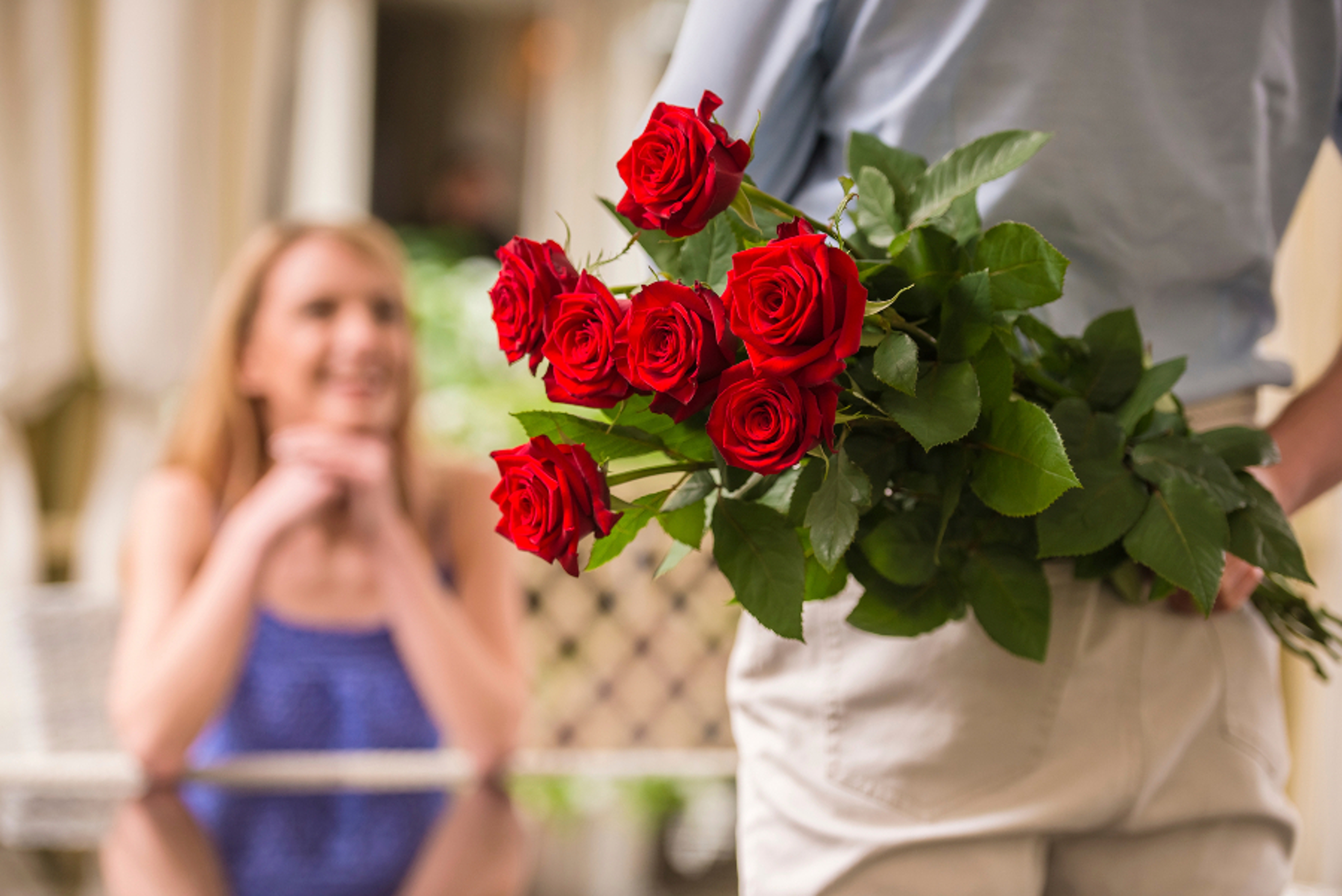 Young woman looking at man with flower bouquet behind the back.