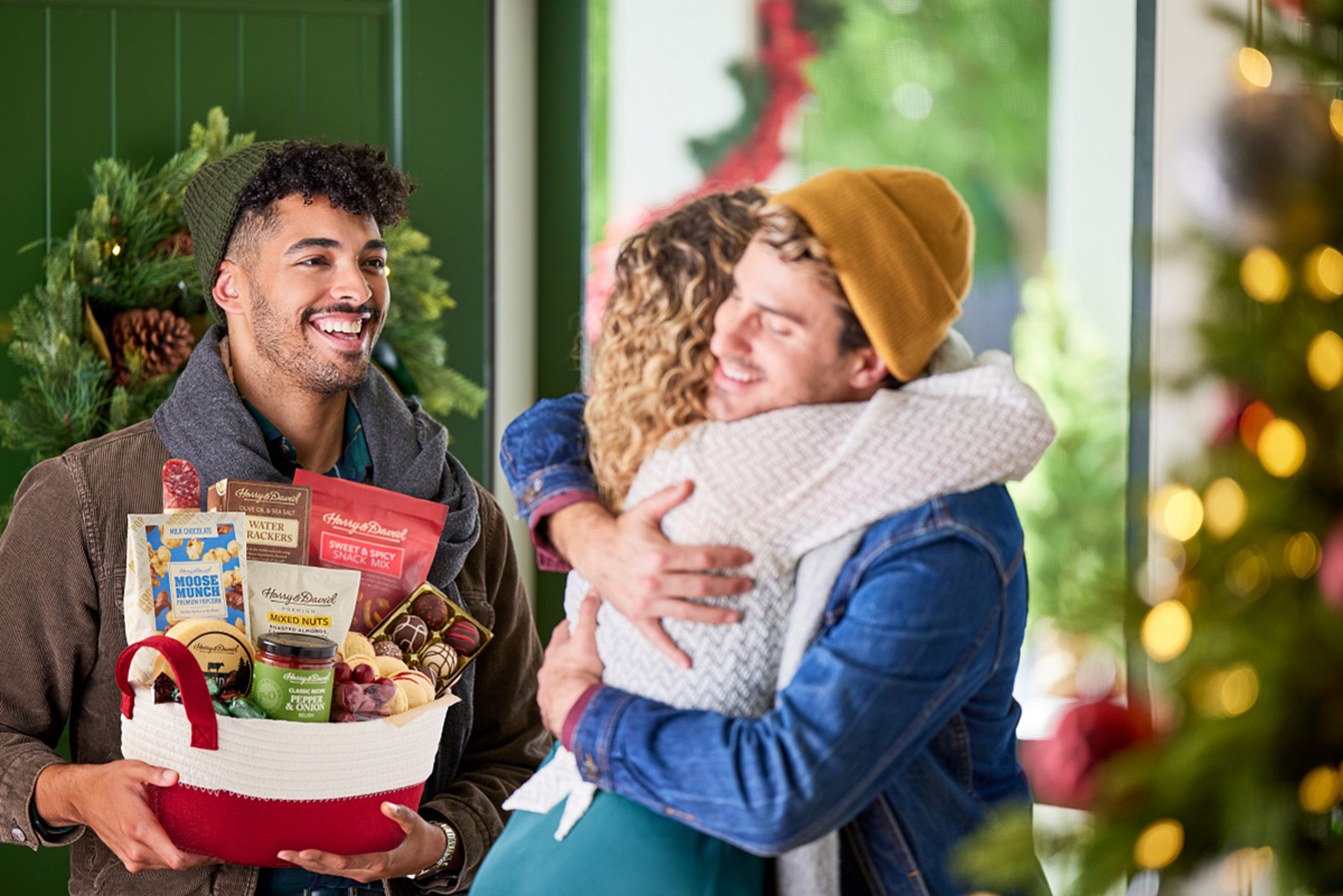 Man and woman hugging while another man smiles at them and holds a gift basket.
