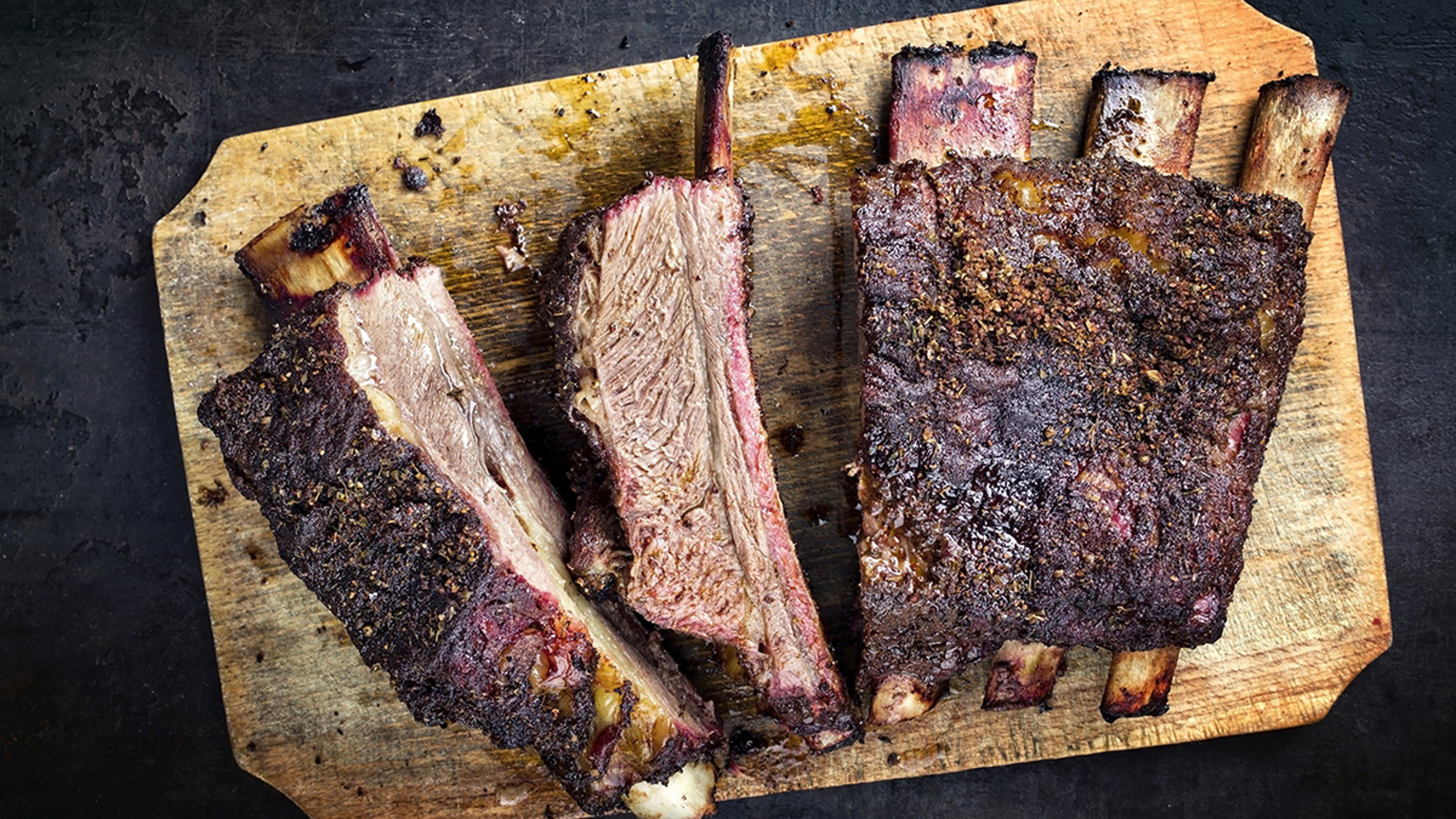 A photo of cuts of beef with a cutting board full of cooked and seasoned beef ribs.