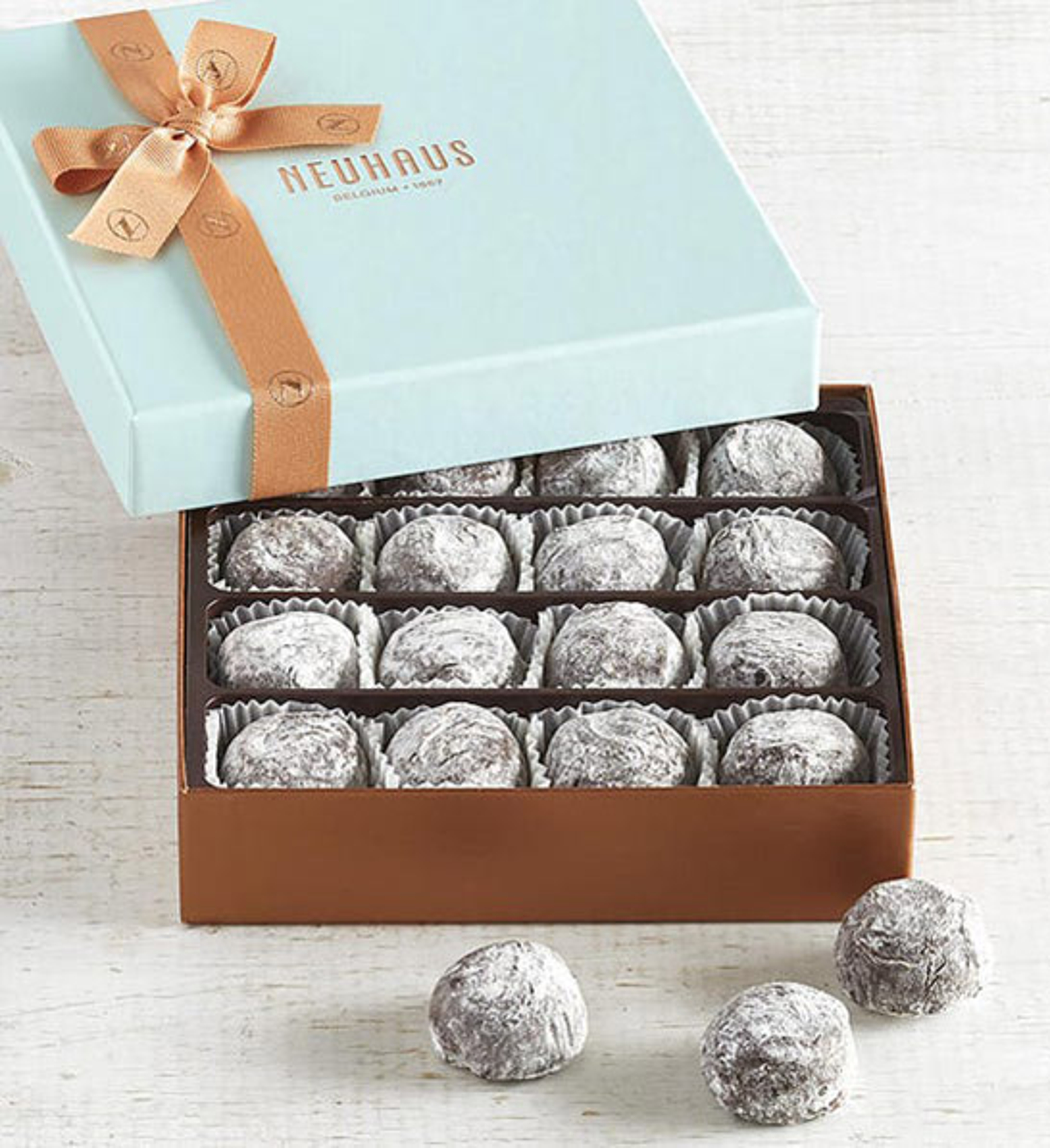 anniversary gift guide image champagne truffles in a gold and blue box with three truffles sitting outside of it.