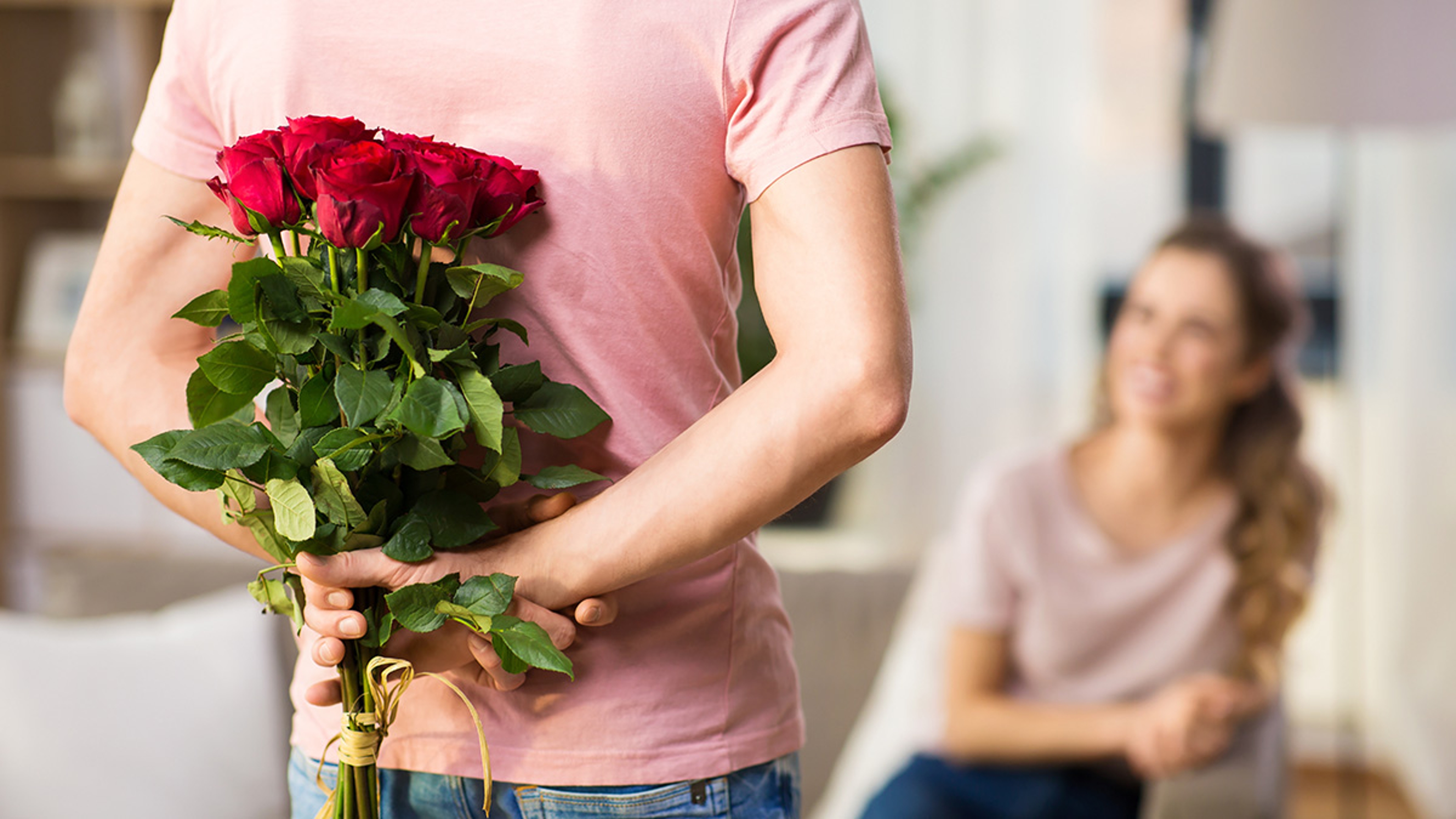 couple, relationships and people concept happy woman looking at man hiding bunch of roses behind his back