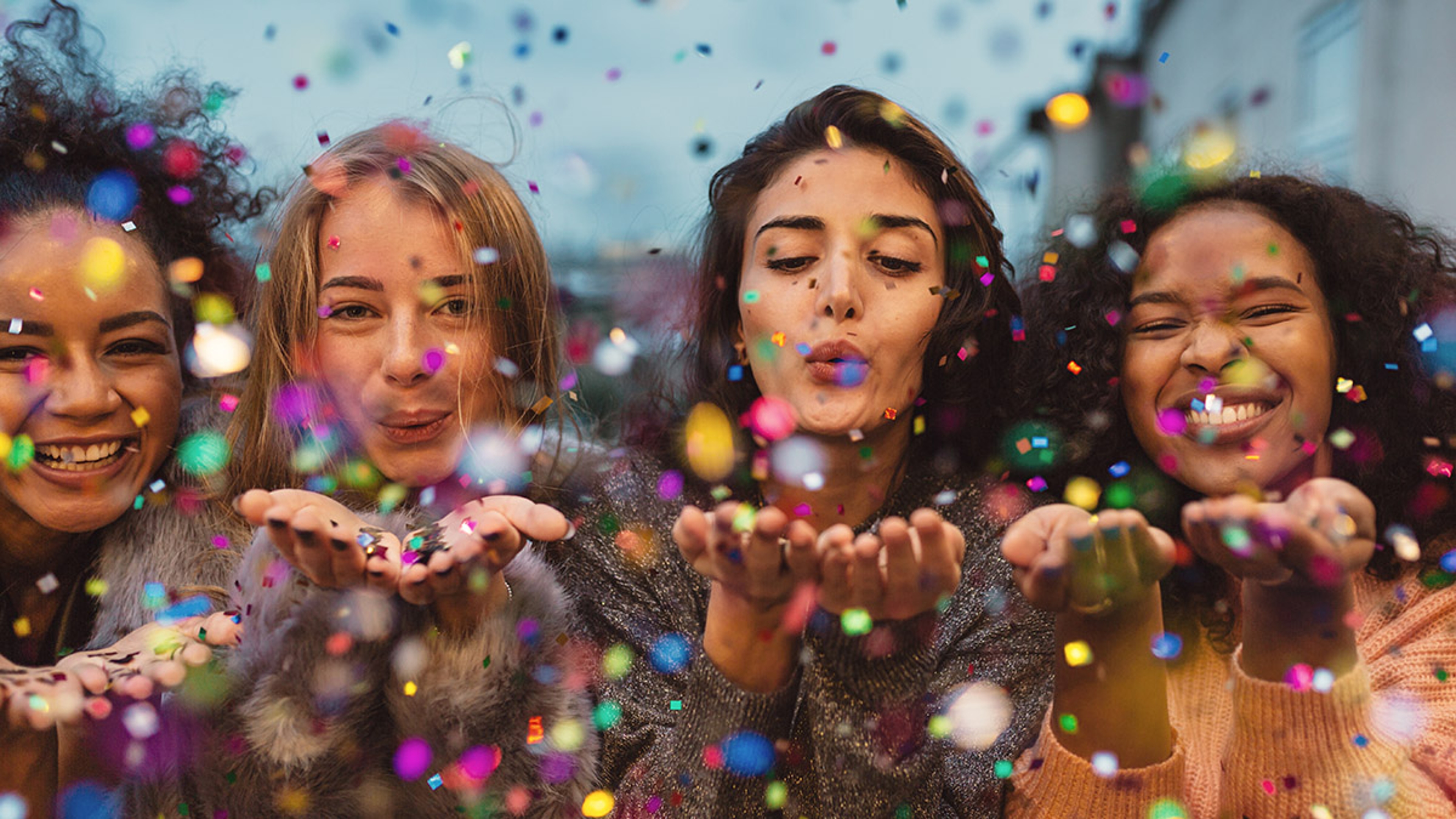 Article Cards Featured Image Young women blowing confetti from hands. Friends celebrating out