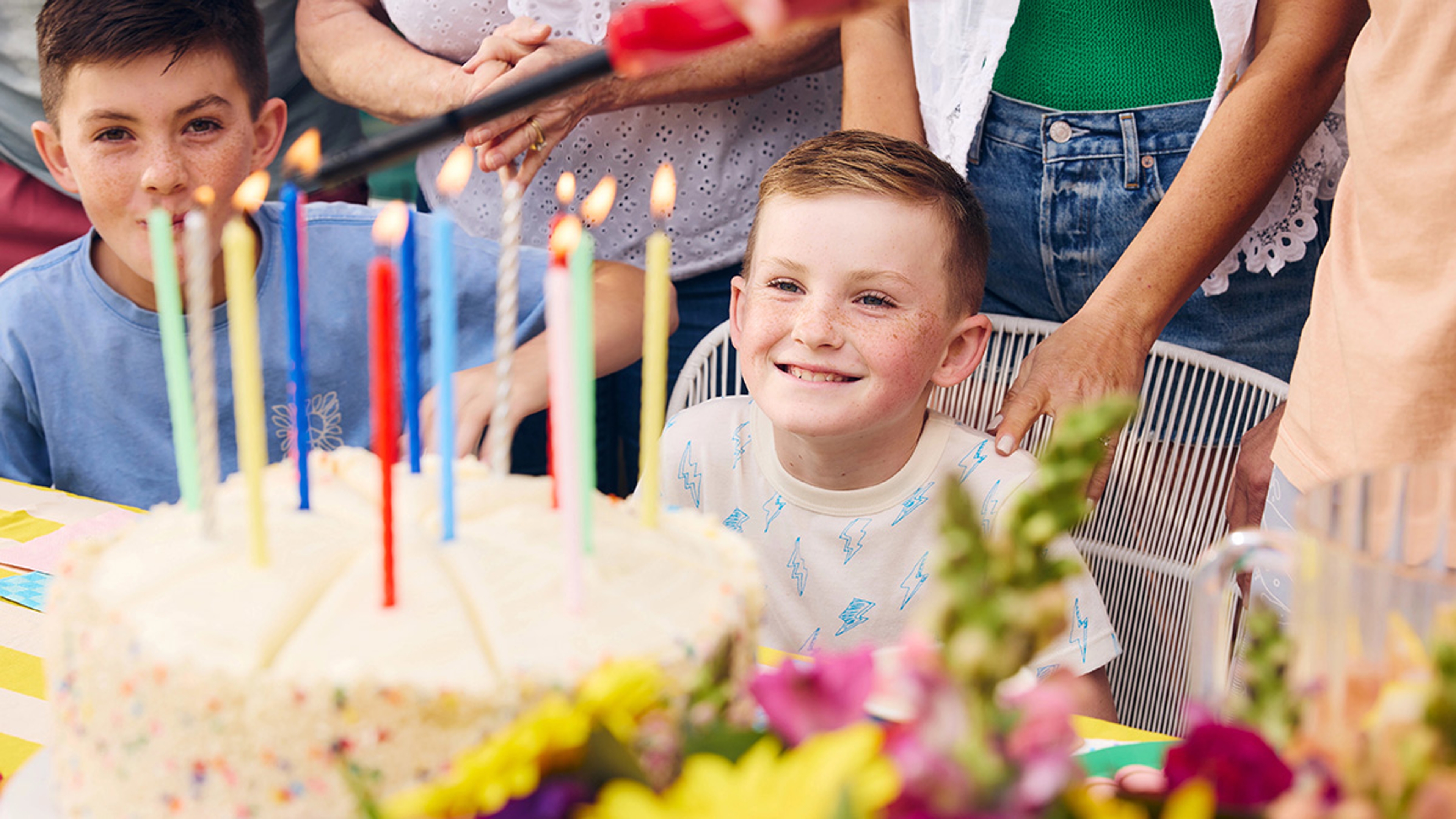 Closeup of boy smiling at birthday cake while people around him sing happy birthday.
