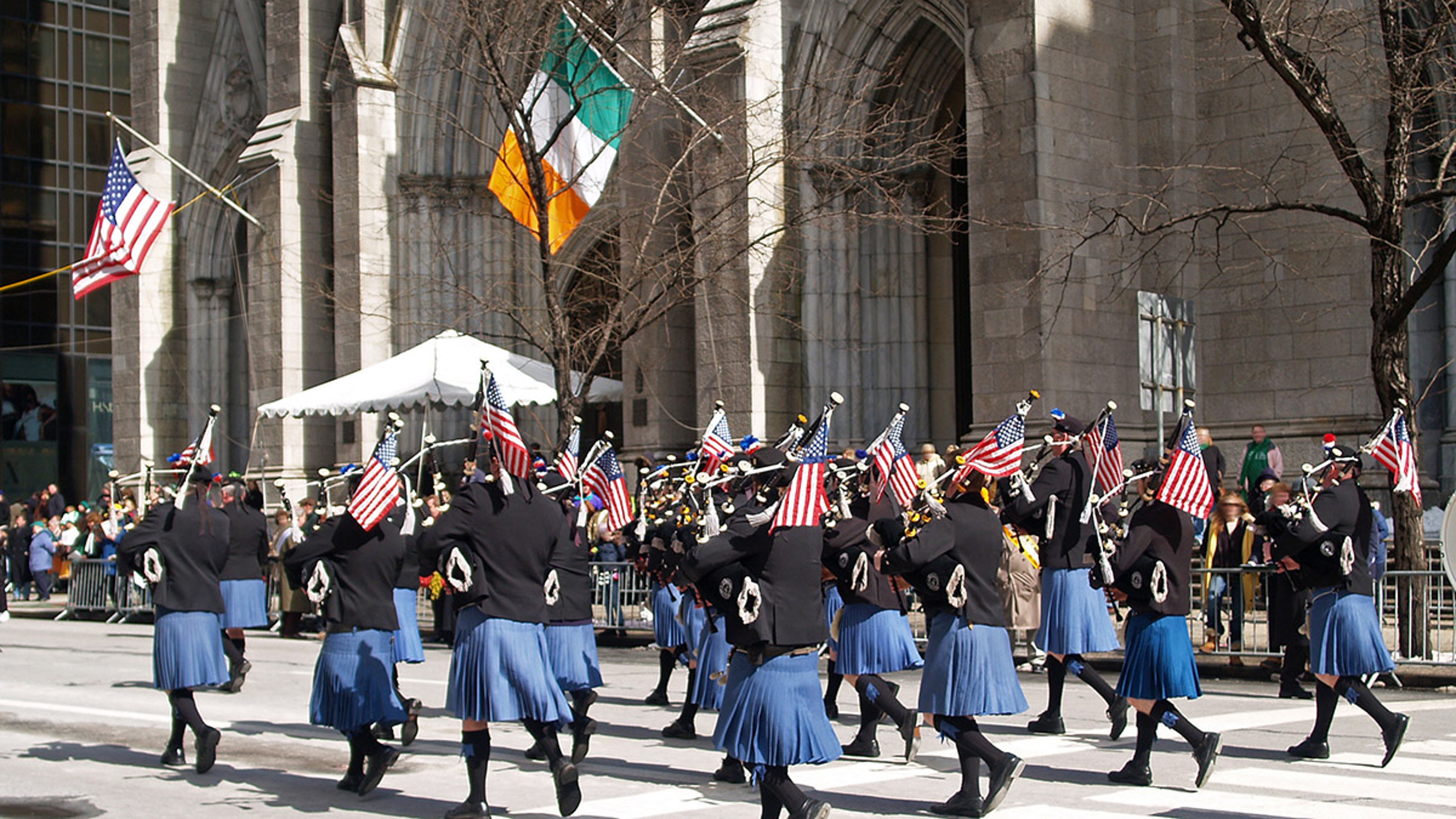 History of St. Patrick's Day with a parade of pipers walking down a street.