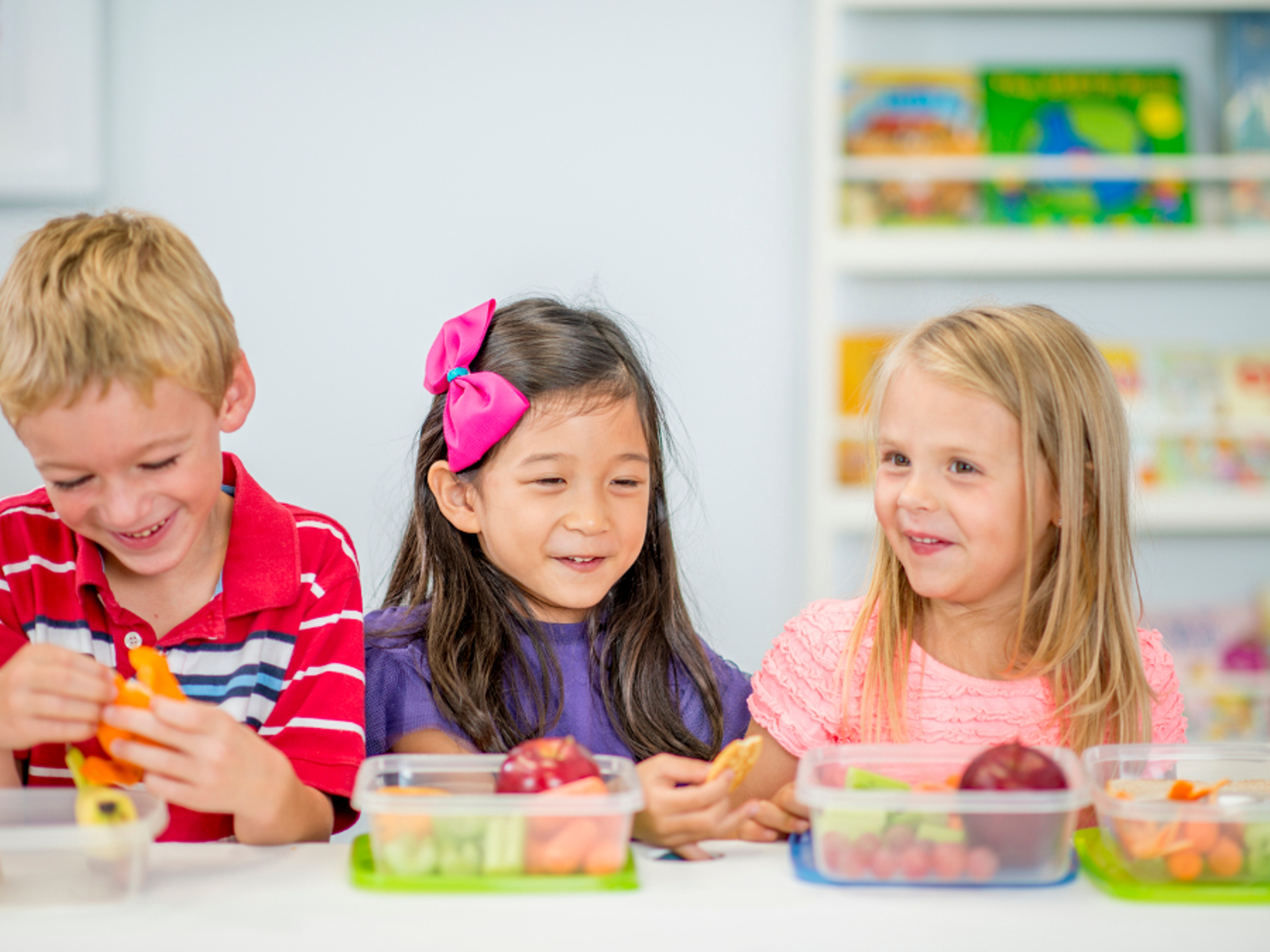 Article Cards Featured Image A multi ehthnic group of elementary age children are sitting together at a table eating their healthy snack full of apples, carrots, and celery.