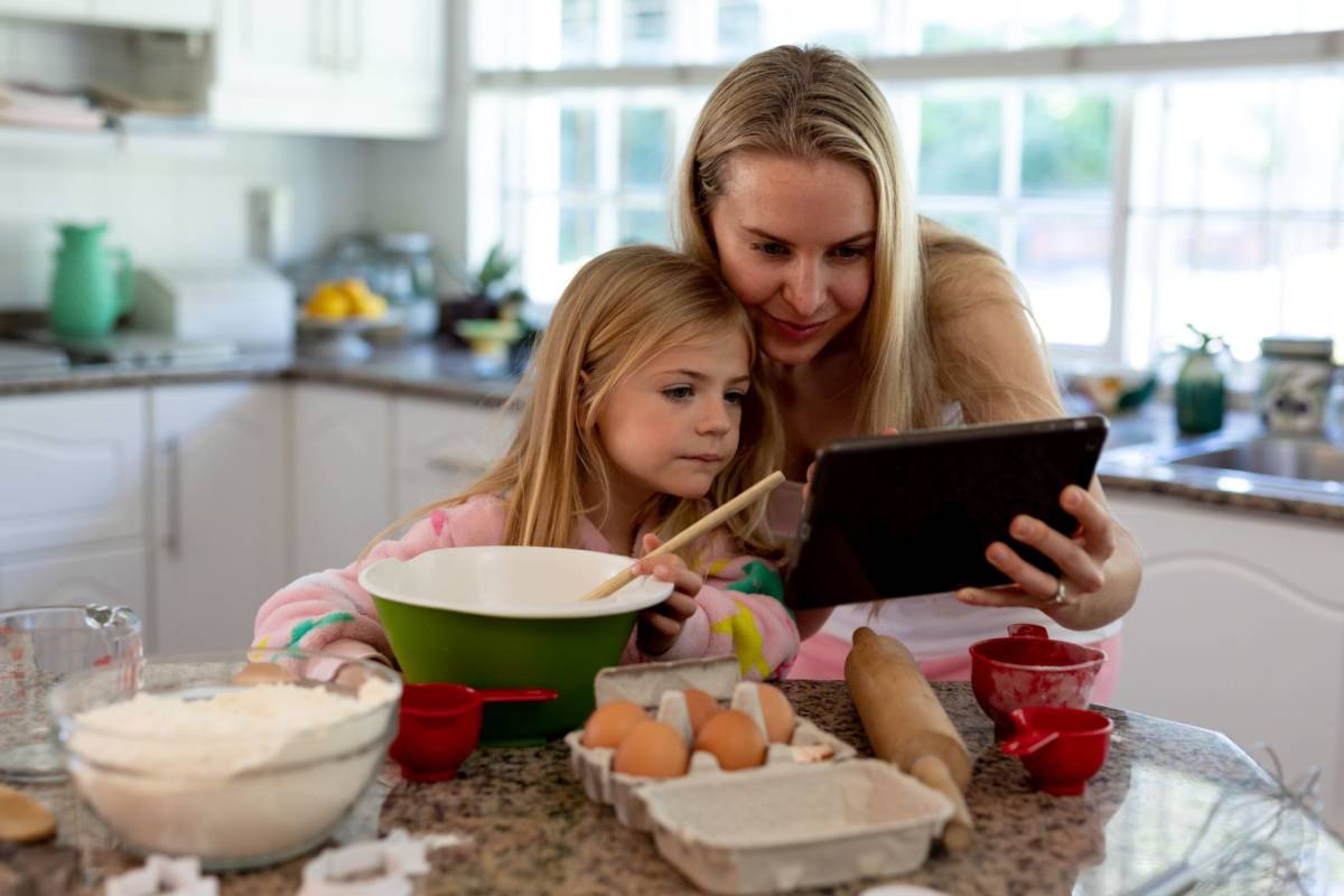 Mother and daughter looking at tablet while cooking in the kitchen