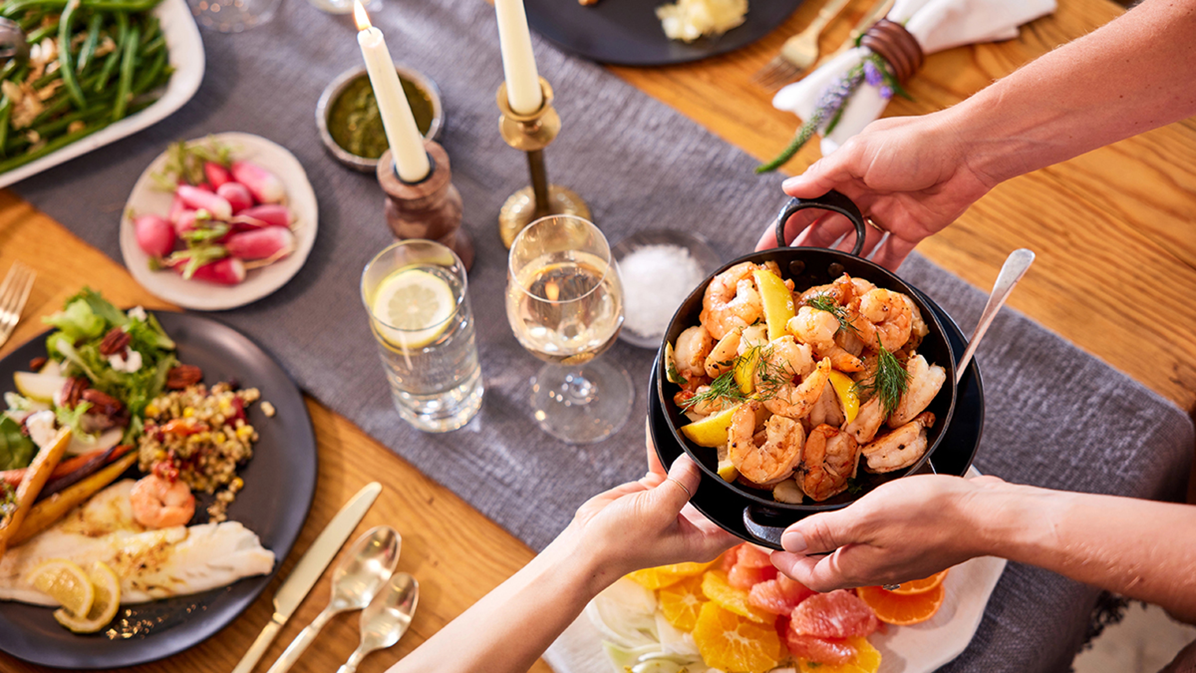 Platter of shrimp being handed to another person at a laid table.