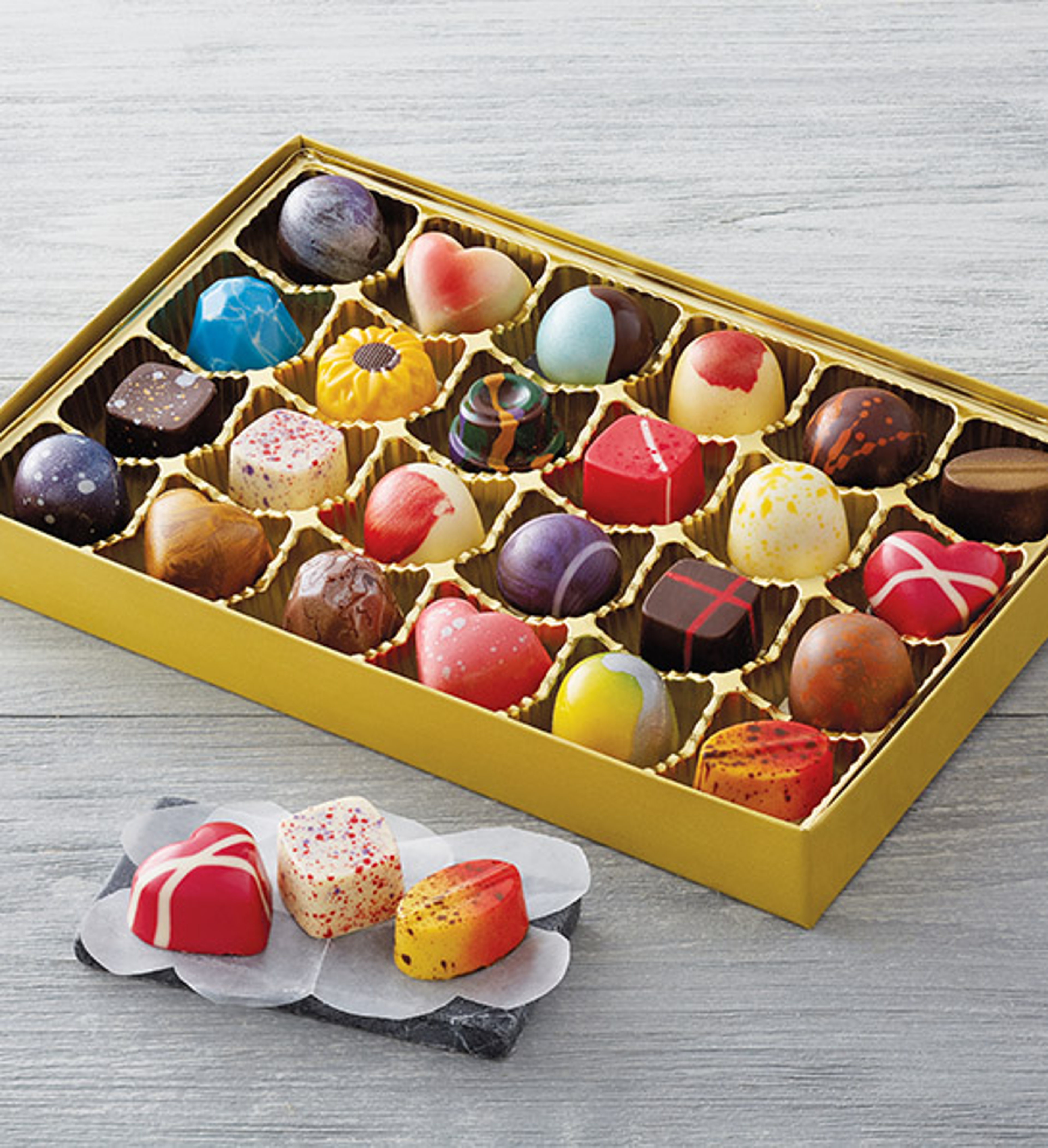 gifts for caregivers image multicolored chocolates in a gold box with three sitting on a napkin outside and in front of the box.