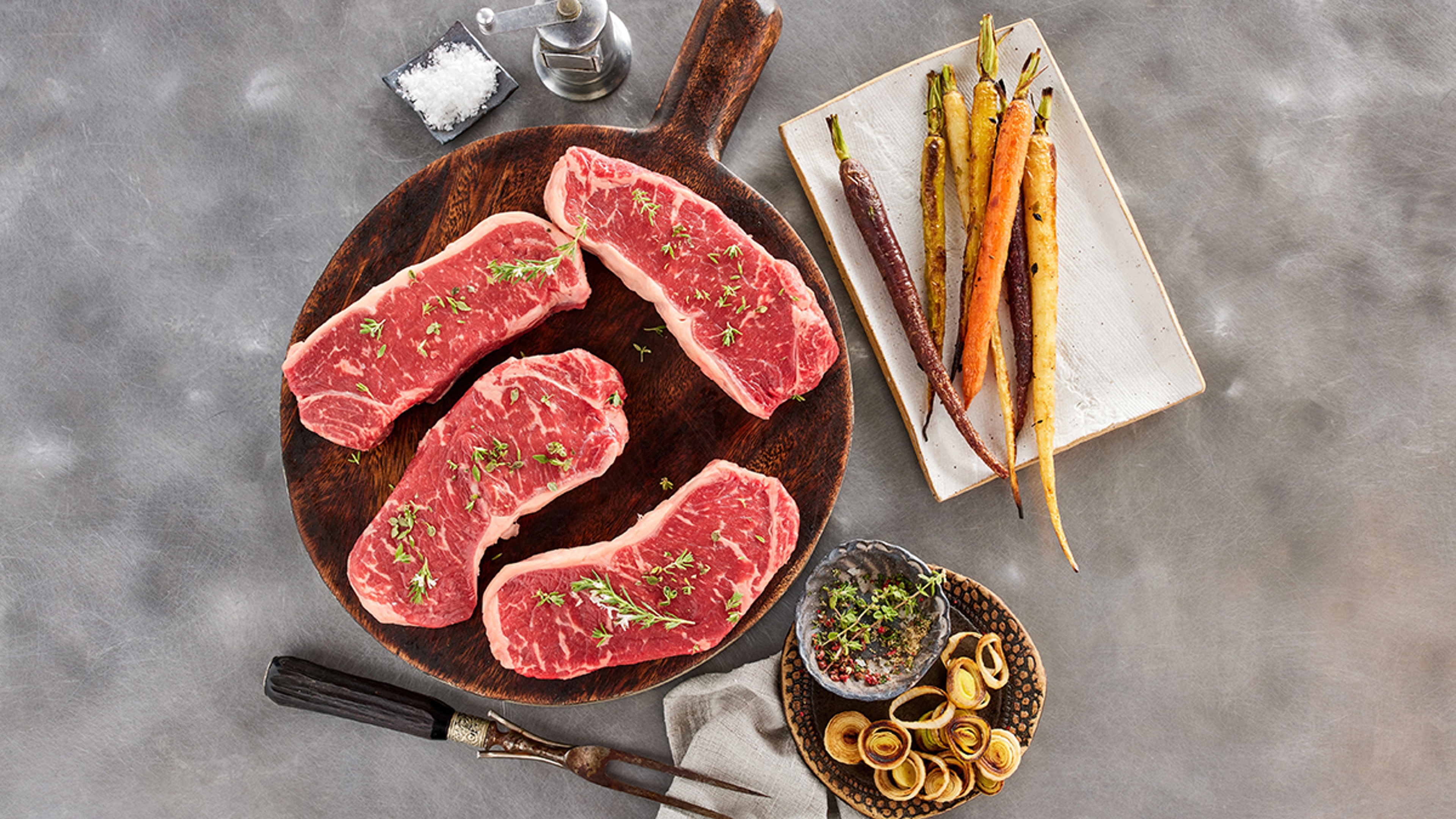 steak recipes with several New York strip steaks on a platter next to roasted carrots.