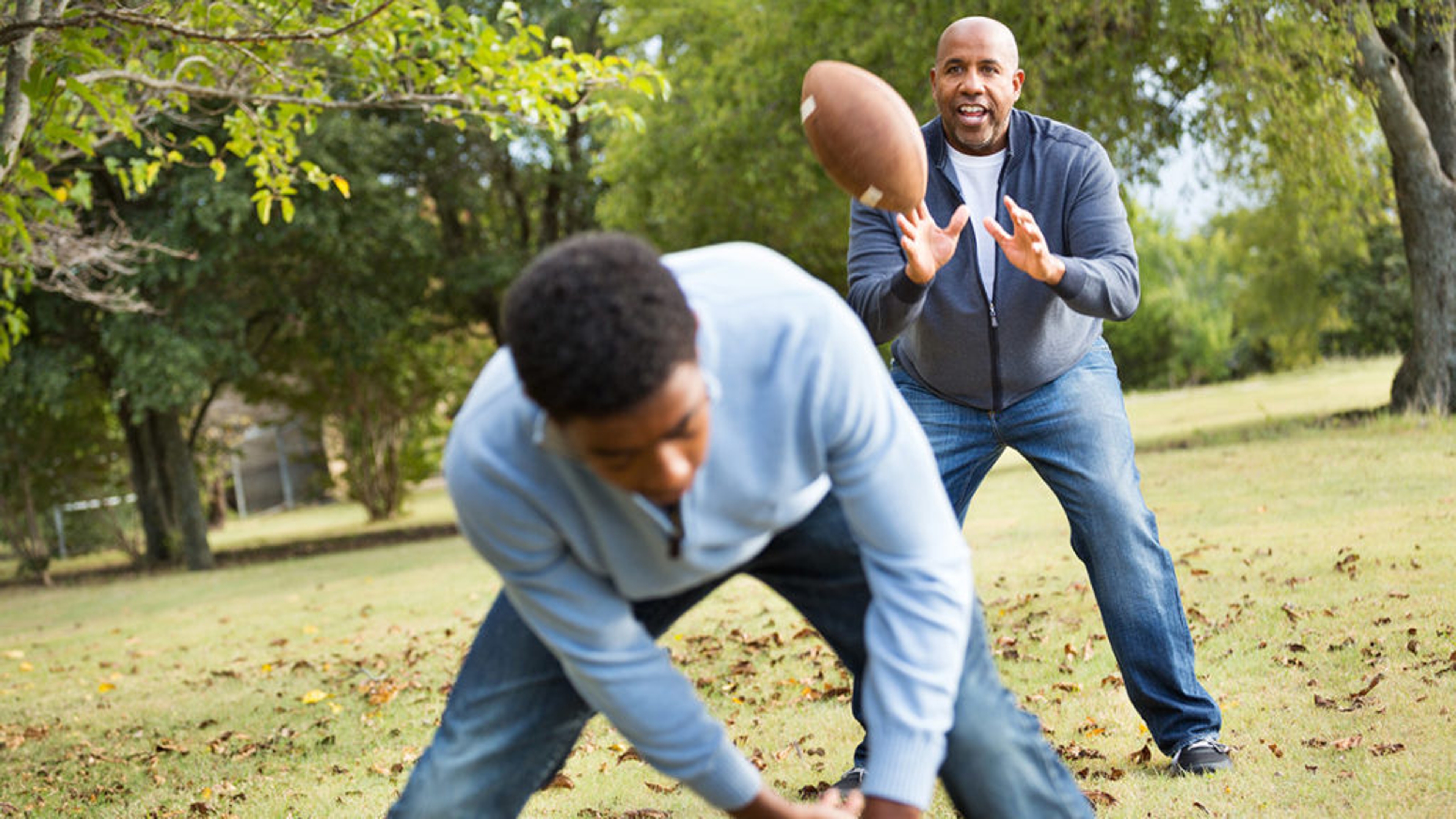 Father and son playing football in a park.