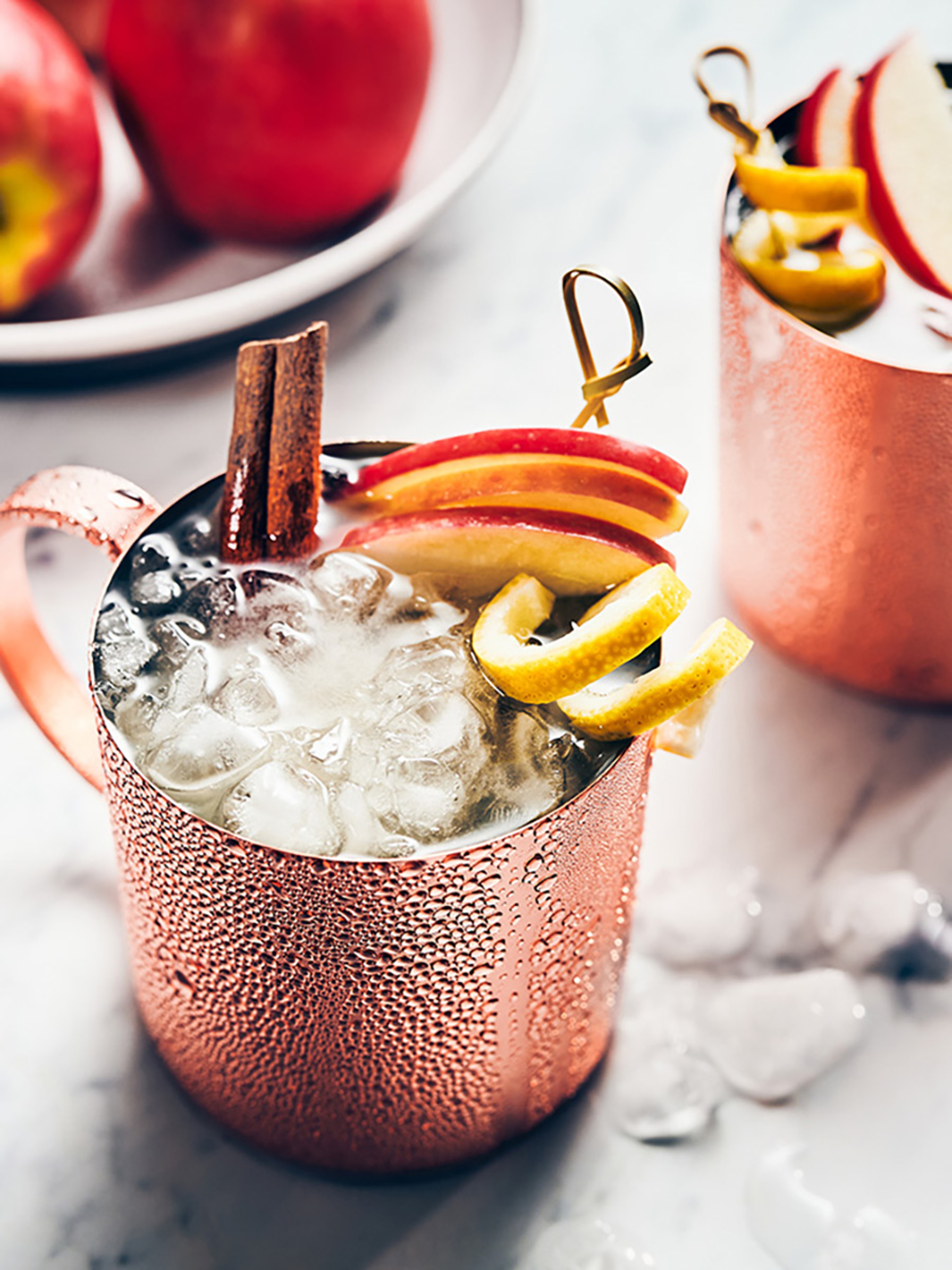 Closeup of a Moscow Mule cocktail with apple slices and a lemon twist.