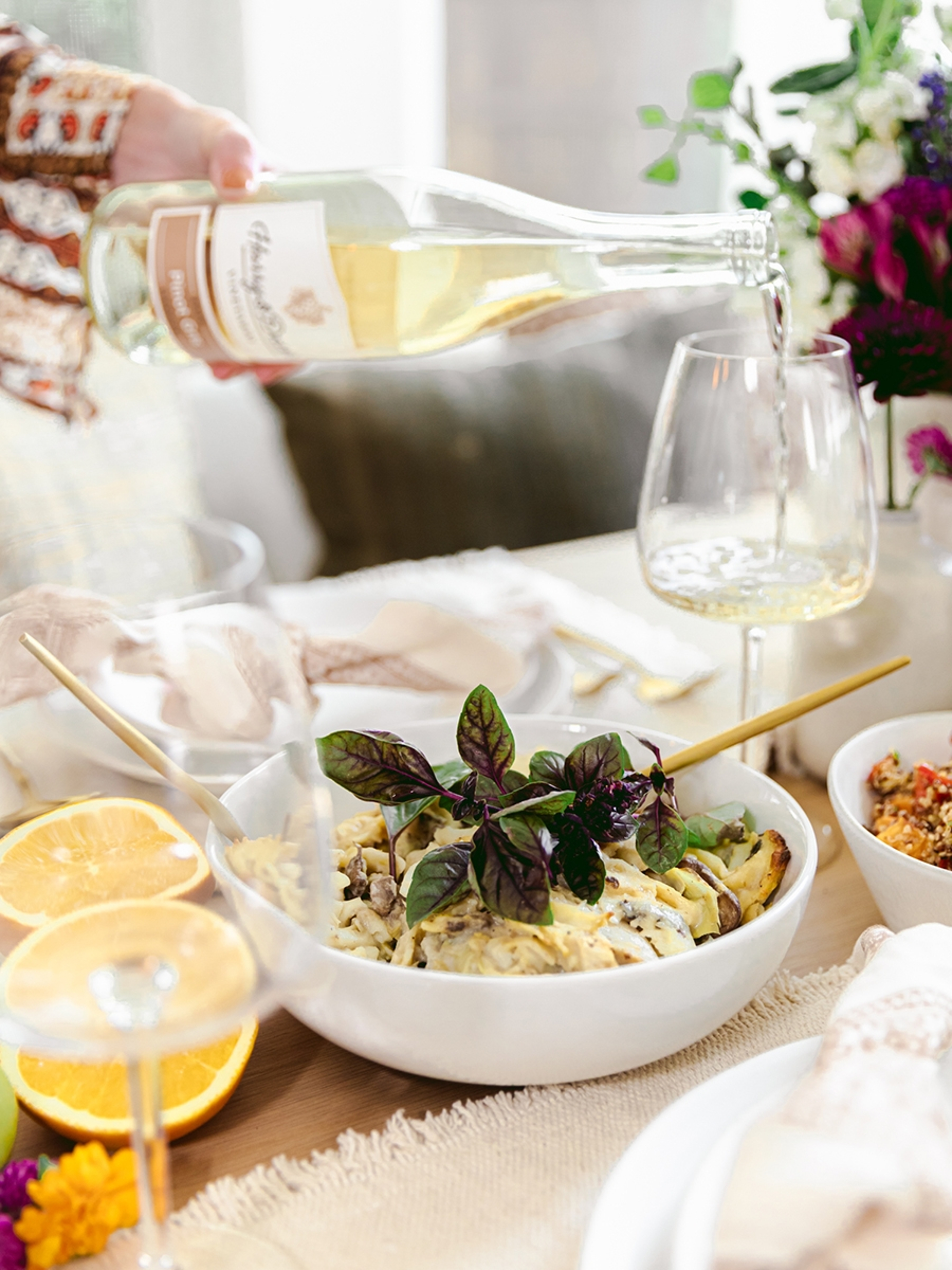A hand pouring wine at a table laid for a Thanksgiving potluck.