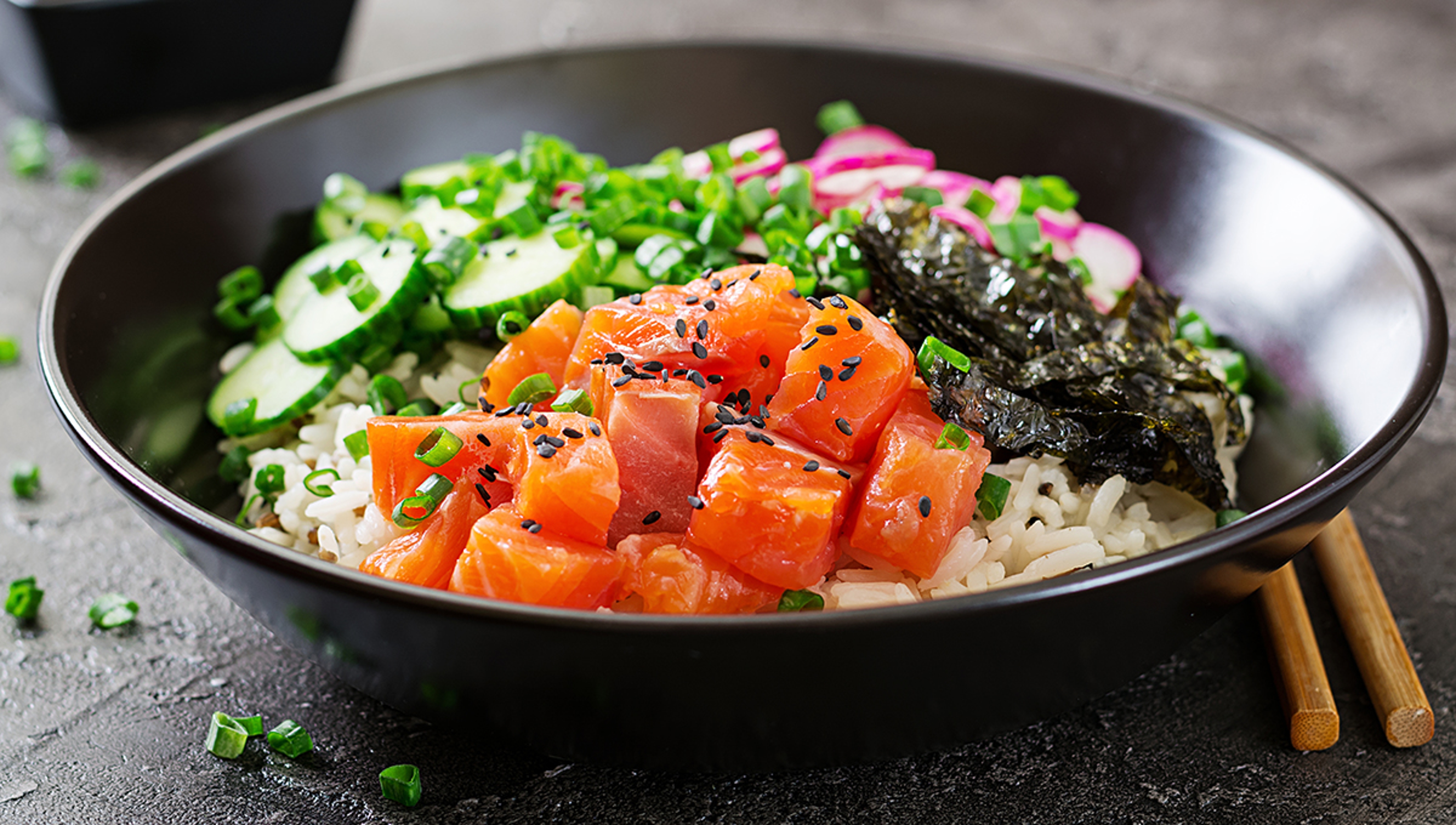 Article Cards Featured Image Hawaiian salmon fish poke bowl with rice, radish,cucumber, tomato, sesame seeds and seaweeds. Buddha bowl. Diet food