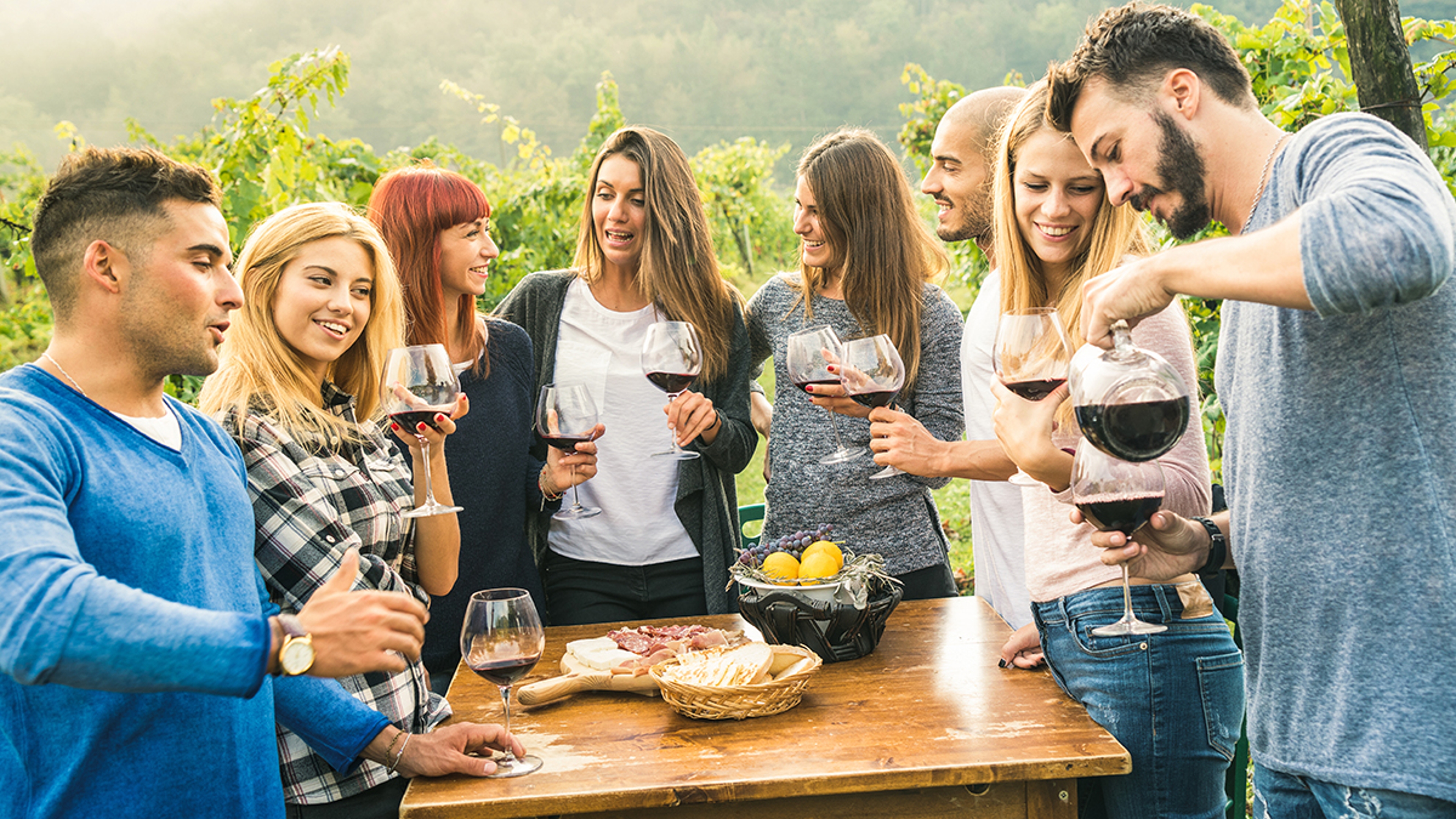 Group of happy friends having fun outdoors drinking red wine   Young people eating local fresh food at grape harvesting in farmhouse vineyard winery   Youth friendship concept on a vivid warm filter