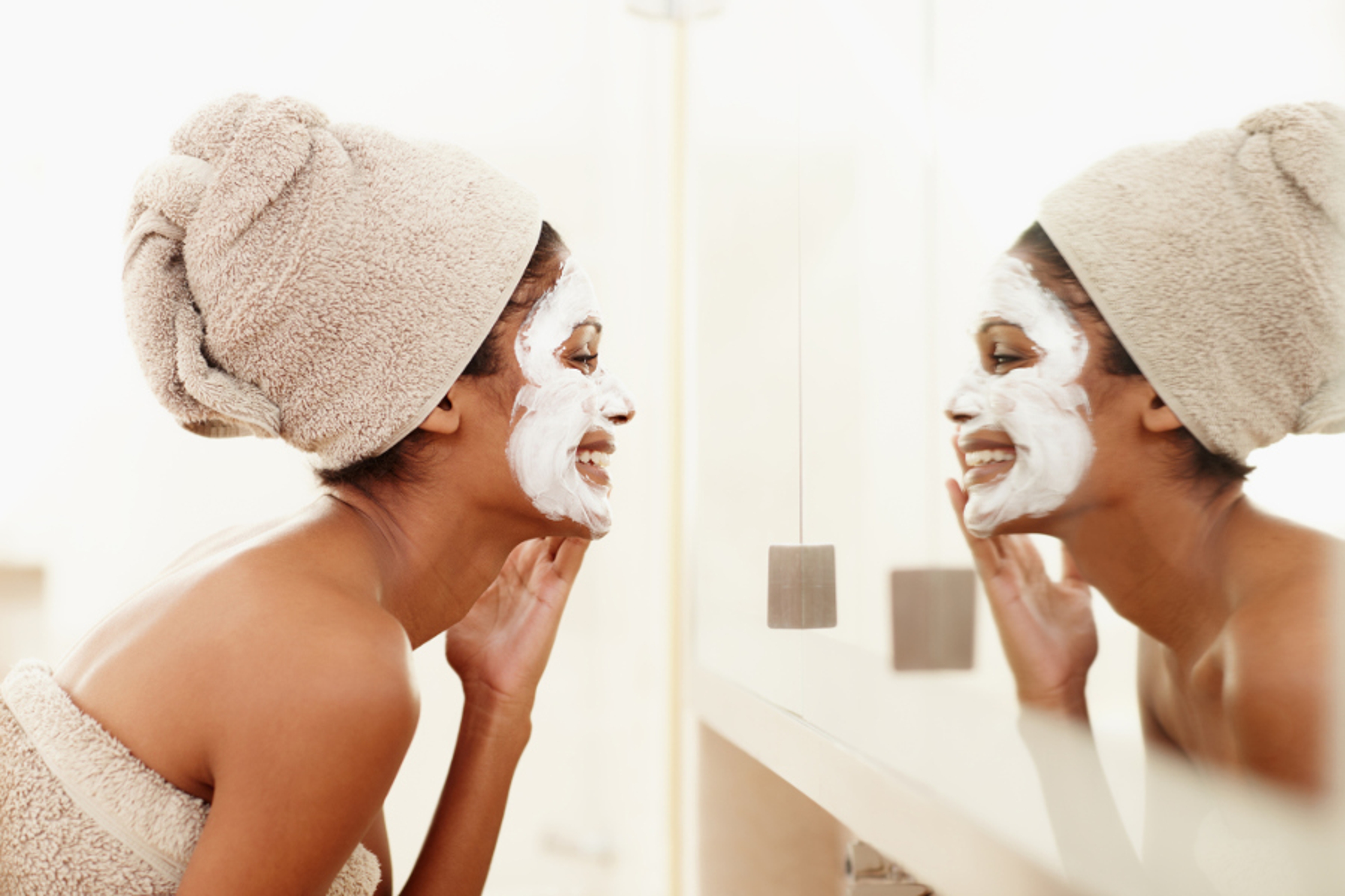 Article Cards Featured Image Mirror reflection of a young ethnic woman laughing and applying a face mask to her face