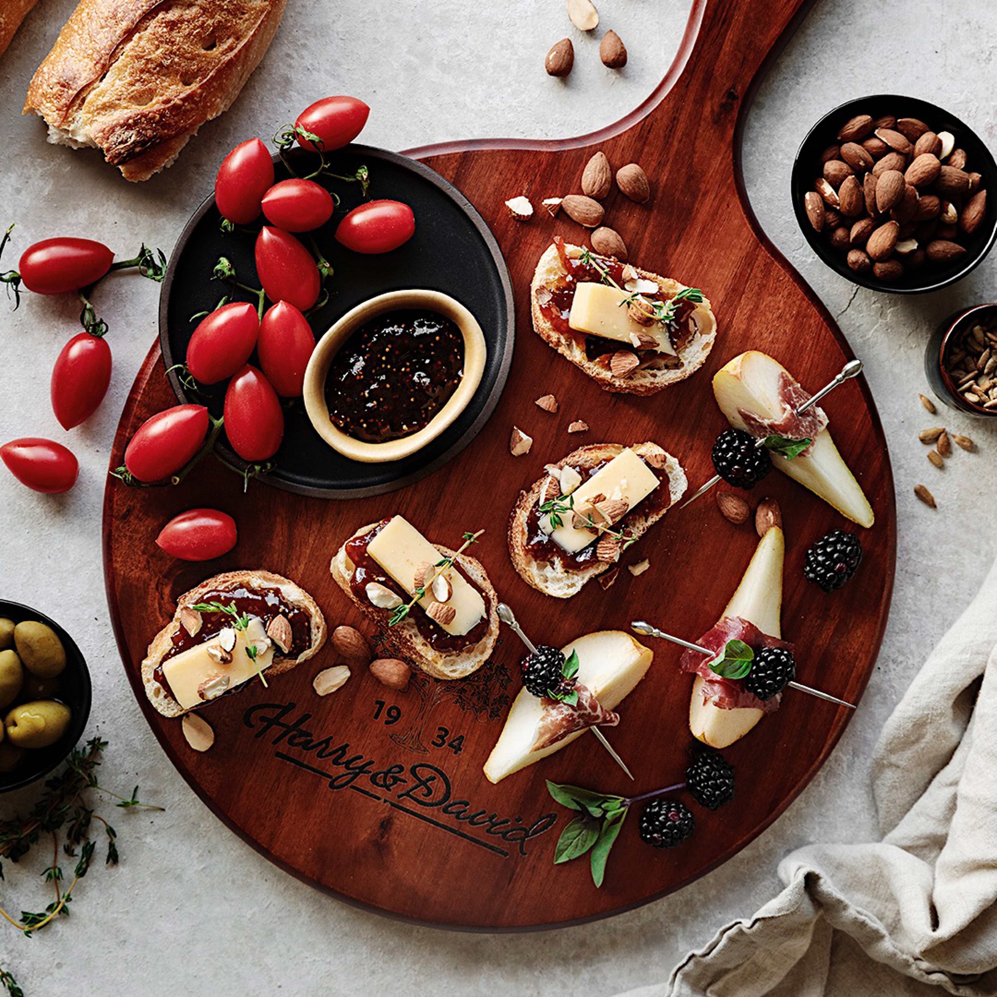 Photo of a charcuterie board with several crostini's and pears wrapped in cured meat with blackberries.