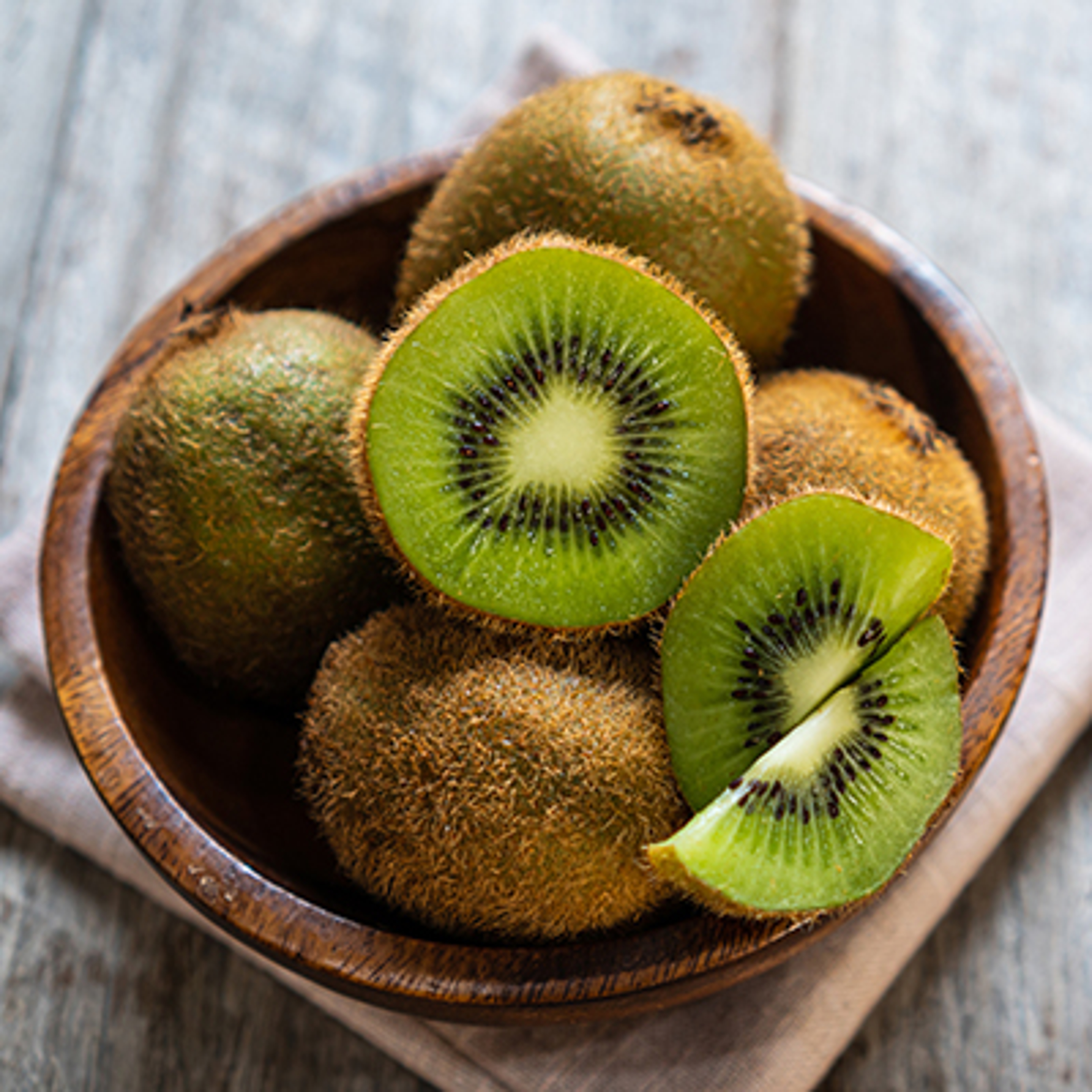 Fresh kiwi fruit in the bowl on wooden background