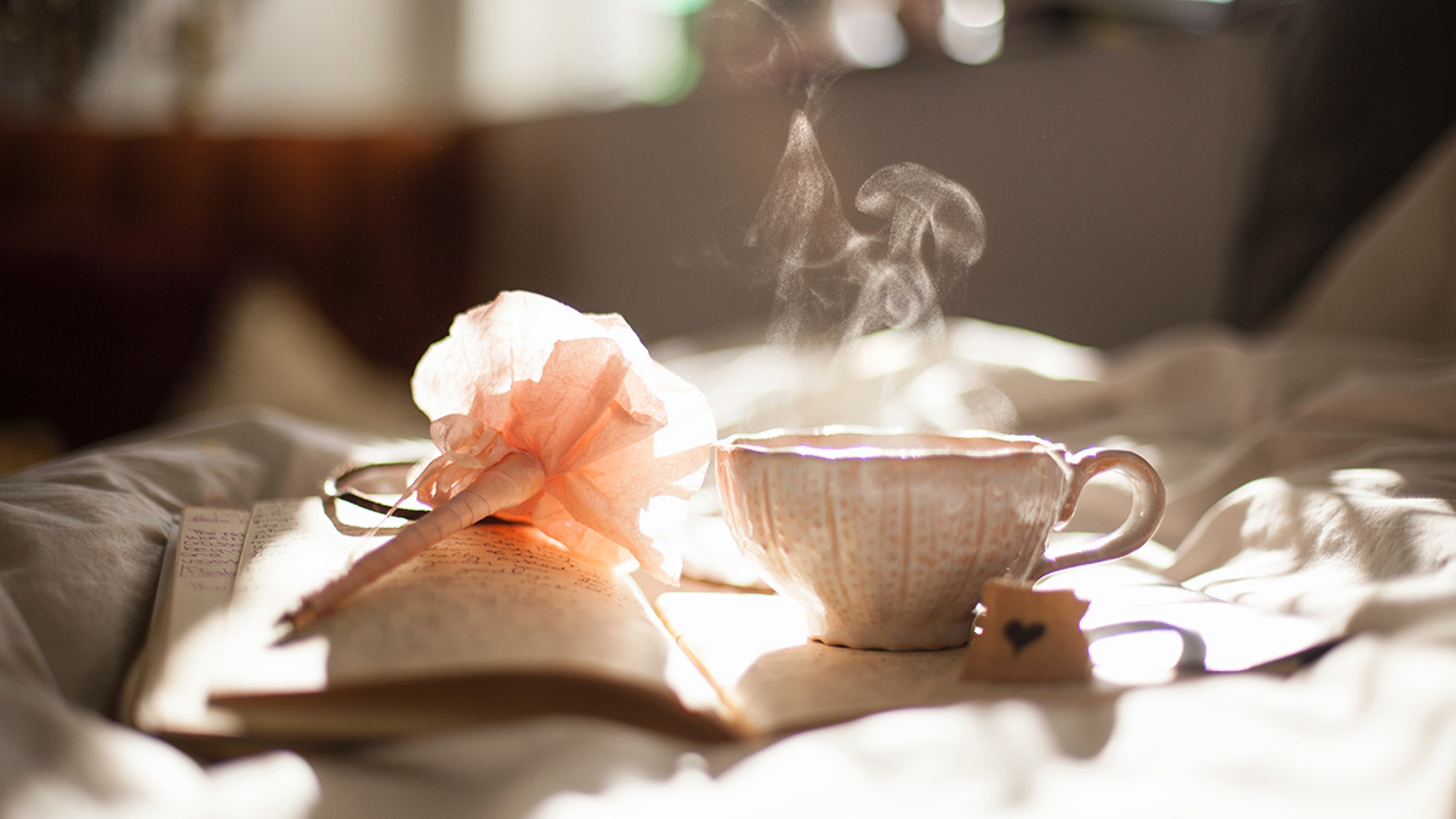 A photo of how to make tea with a cup of steaming tea on a notebook with a pen next to it.