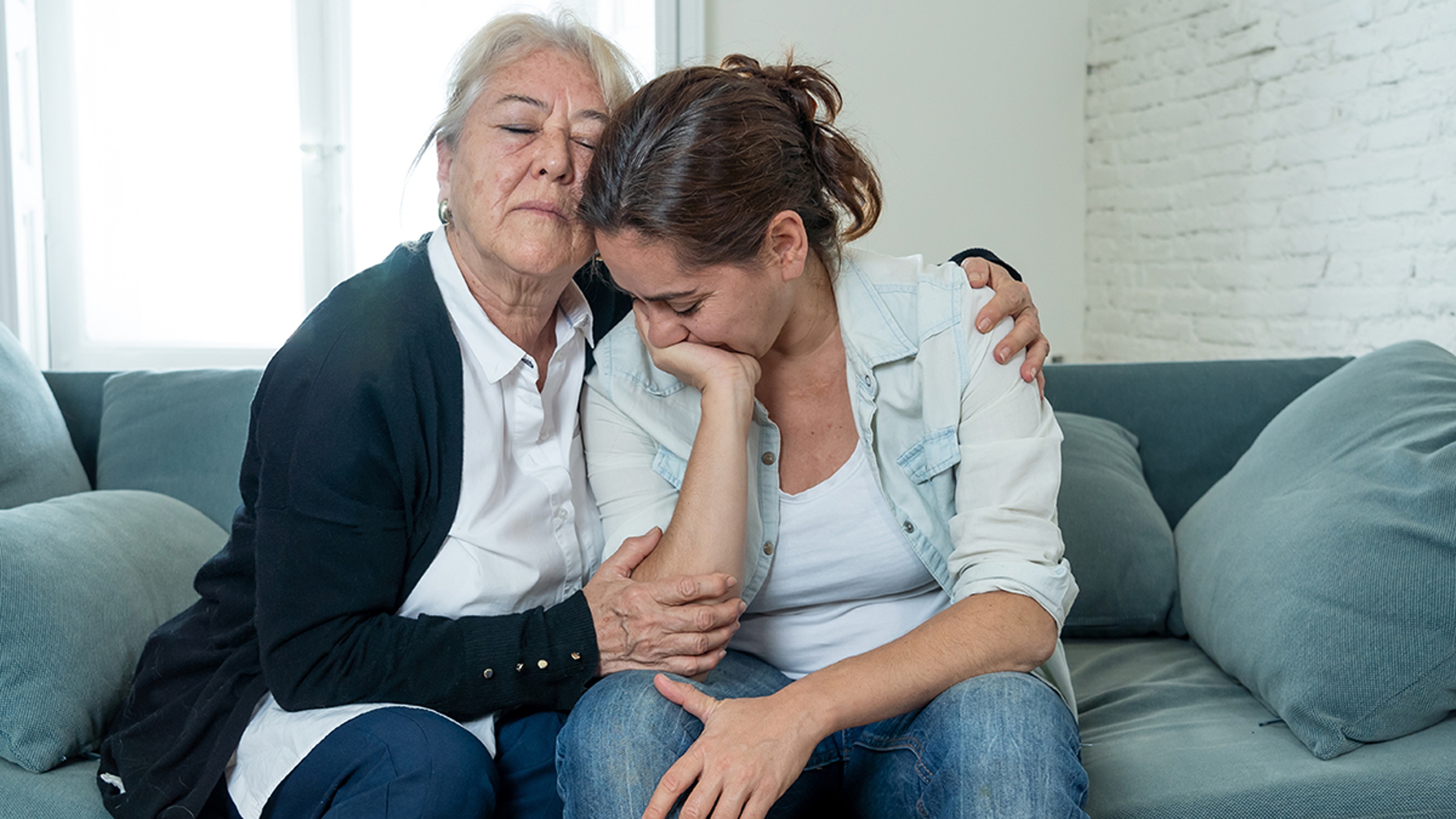 Grief overload with a mother and daughter crying on a couch.