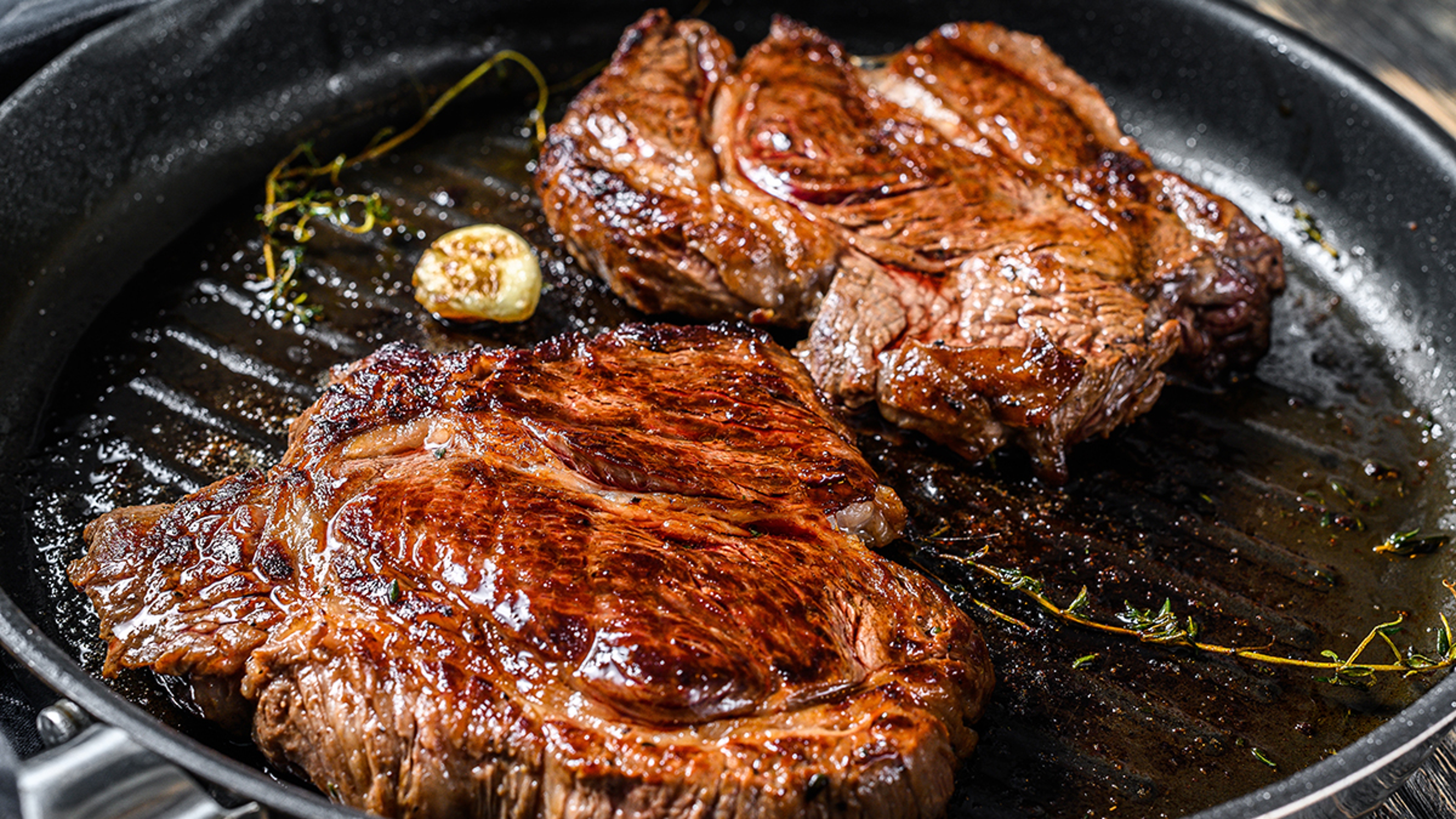 A photo of cuts of beef with two pieces of beef chuck cooking in a cast iron pan.