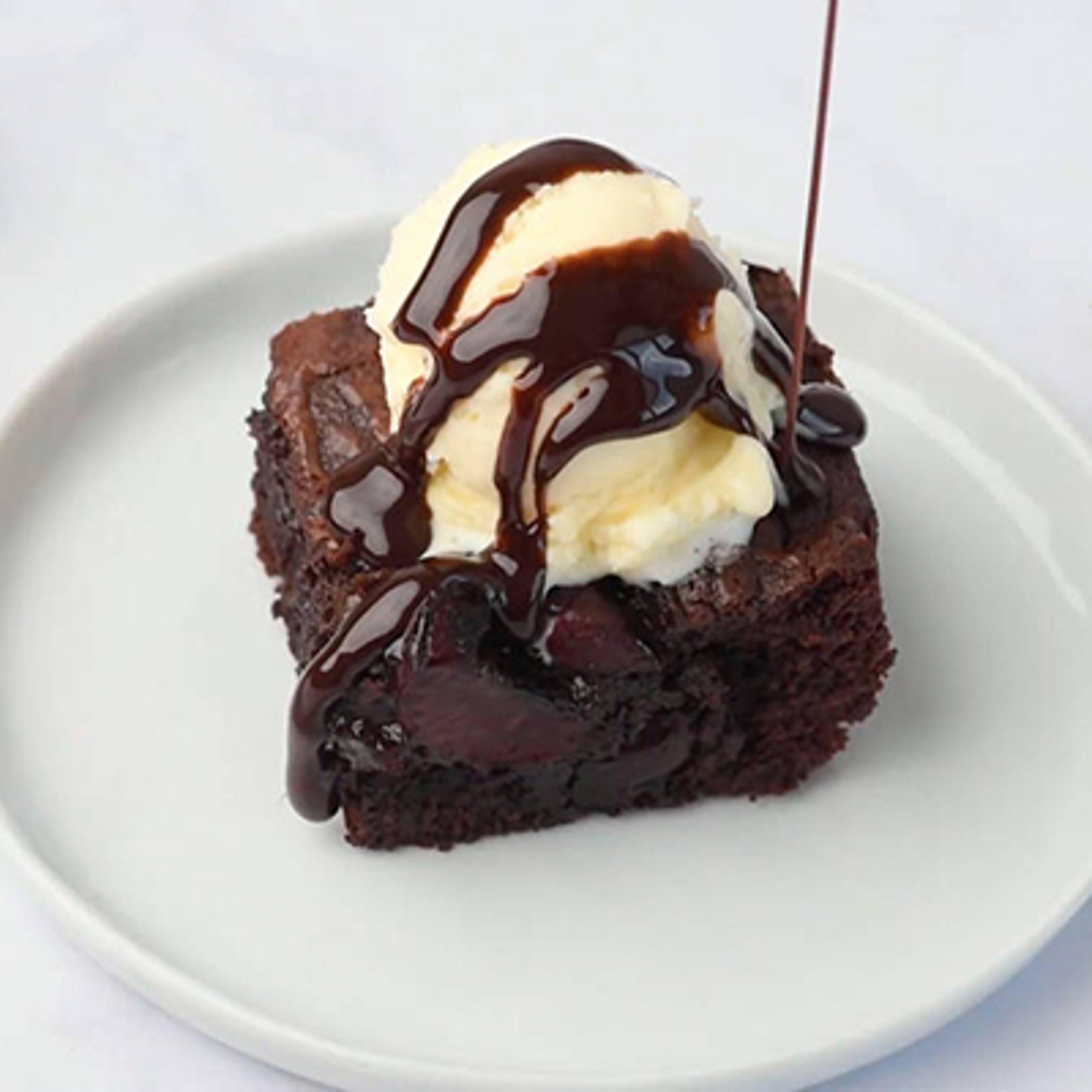 Game day recipes with a cherry brownie topped with ice cream and chocolate sauce on a plate.