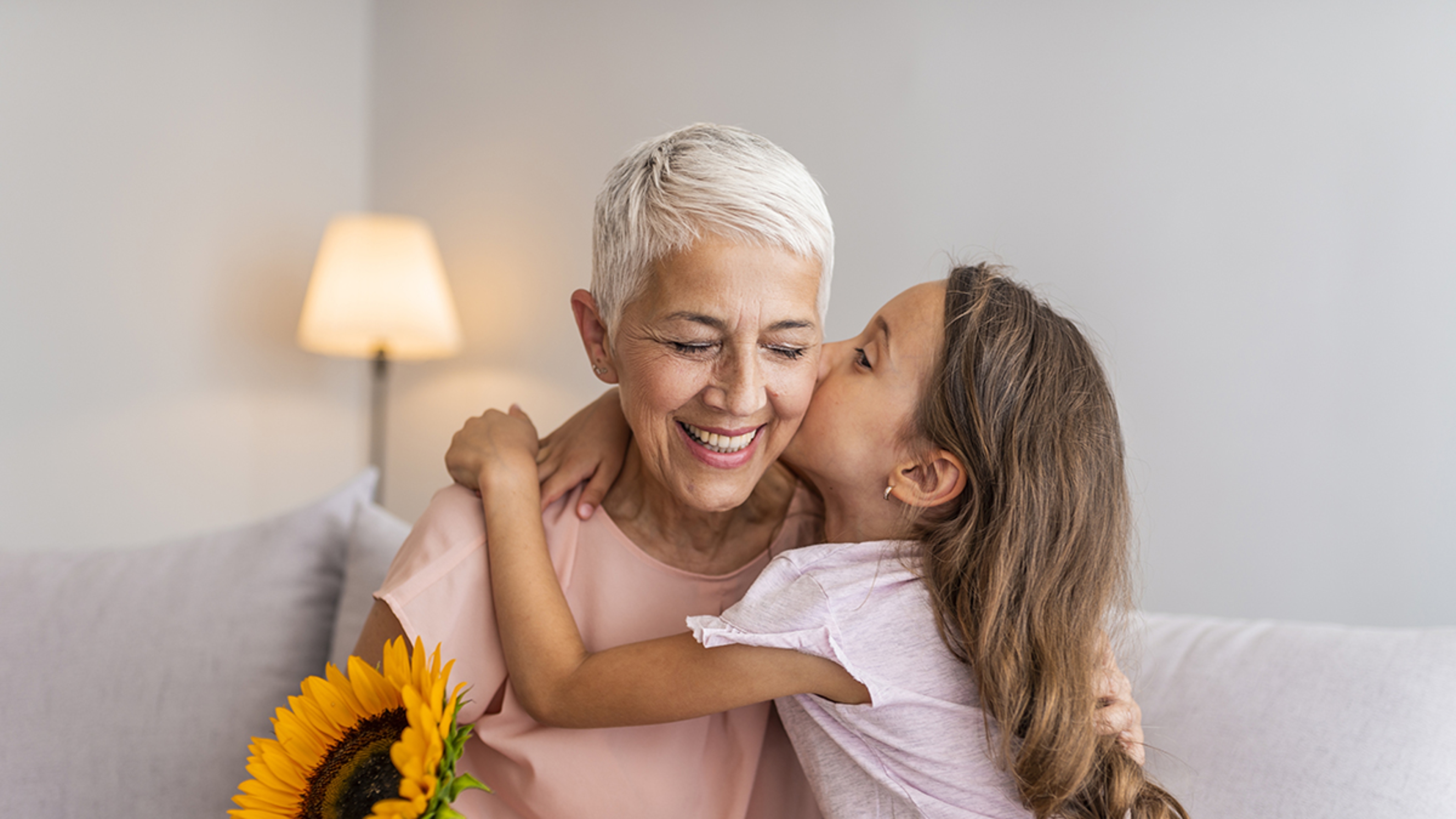 Article Cards Featured Image Happy grandmother hugging small cute grandchild thanking for flowers presented, excited granny embrace granddaughter congratulating her with birthday, making surprise presenting bouquet